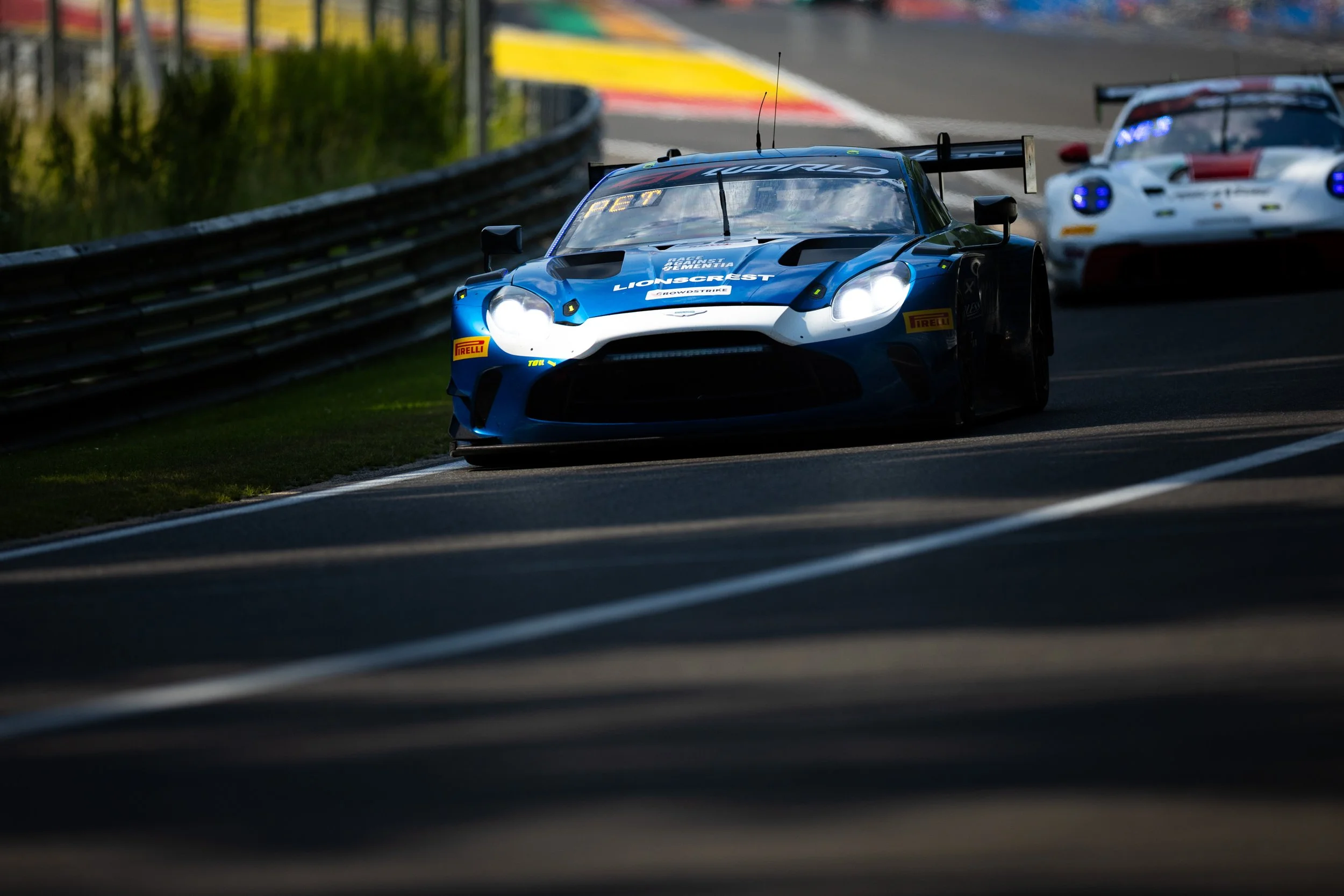 Race cars speeding on a race track surrounded by barriers and greenery.
