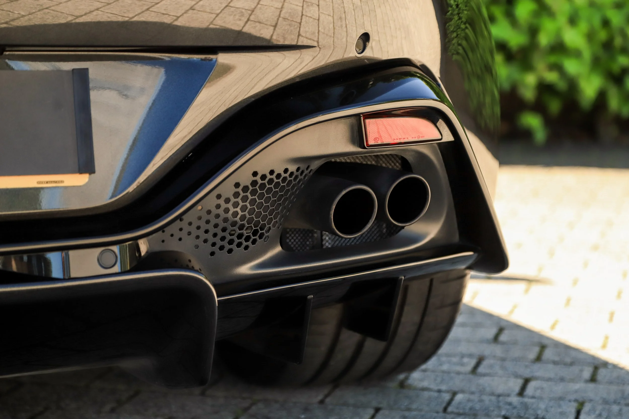 Close-up of the rear end of a black luxury sports car, focusing on dual exhaust pipes and a part of the rear tire.