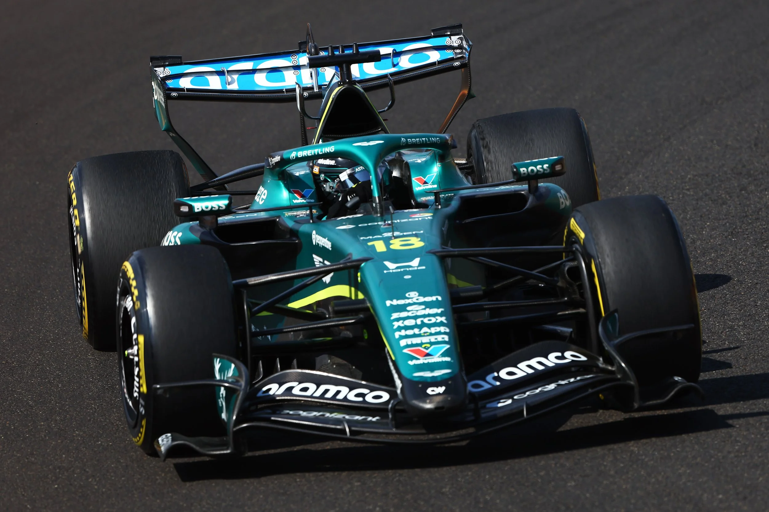 A teal and black Formula 1 race car with sponsor logos, racing on a dark asphalt track.