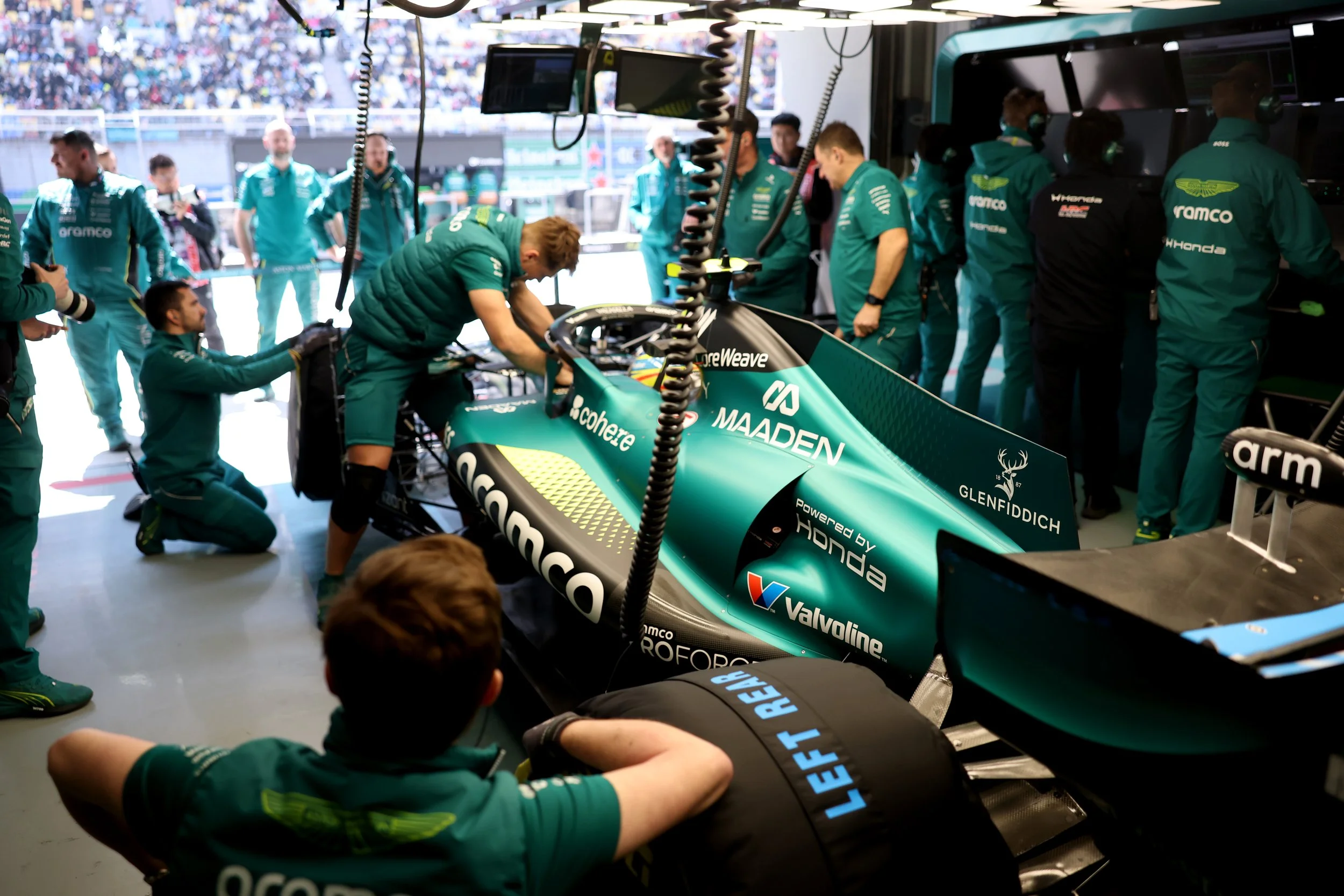 Formula 1 racing team members working on a race car in the garage during a race event.