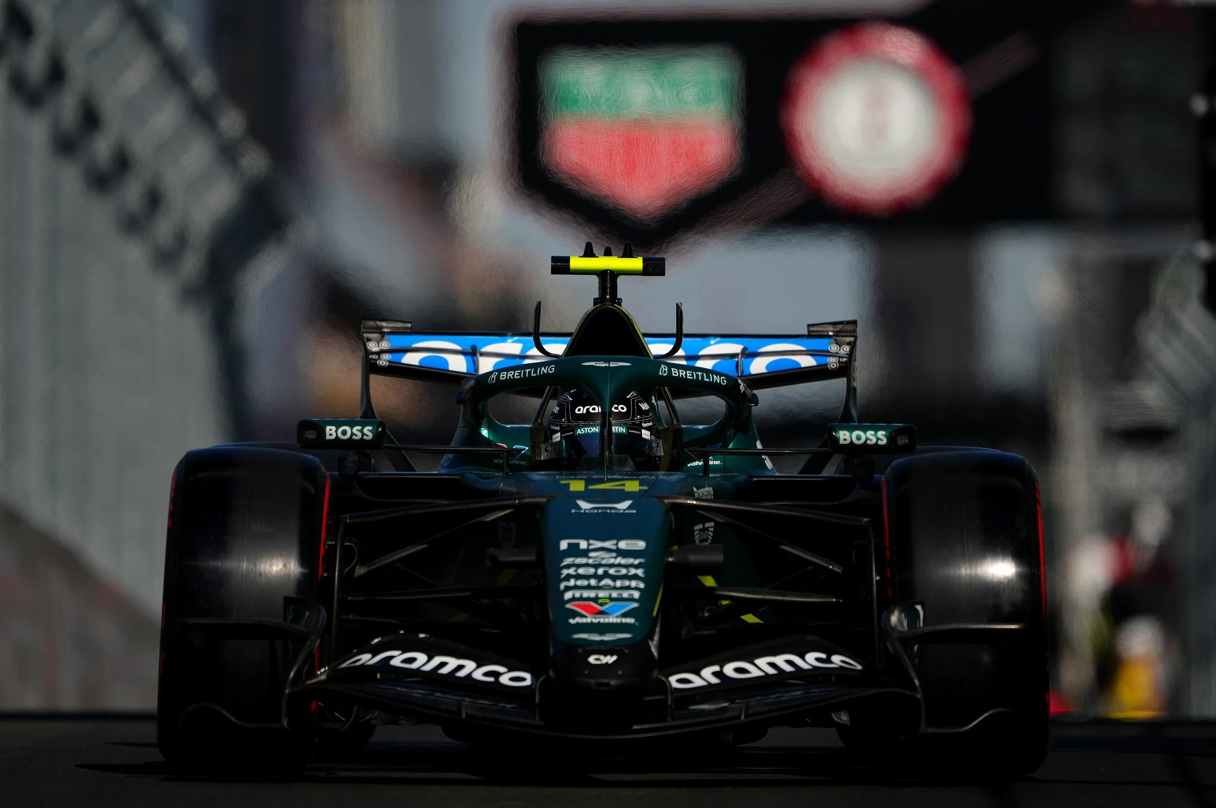 A racing car on a track, viewed from front, with a blurred background of another race car and track.