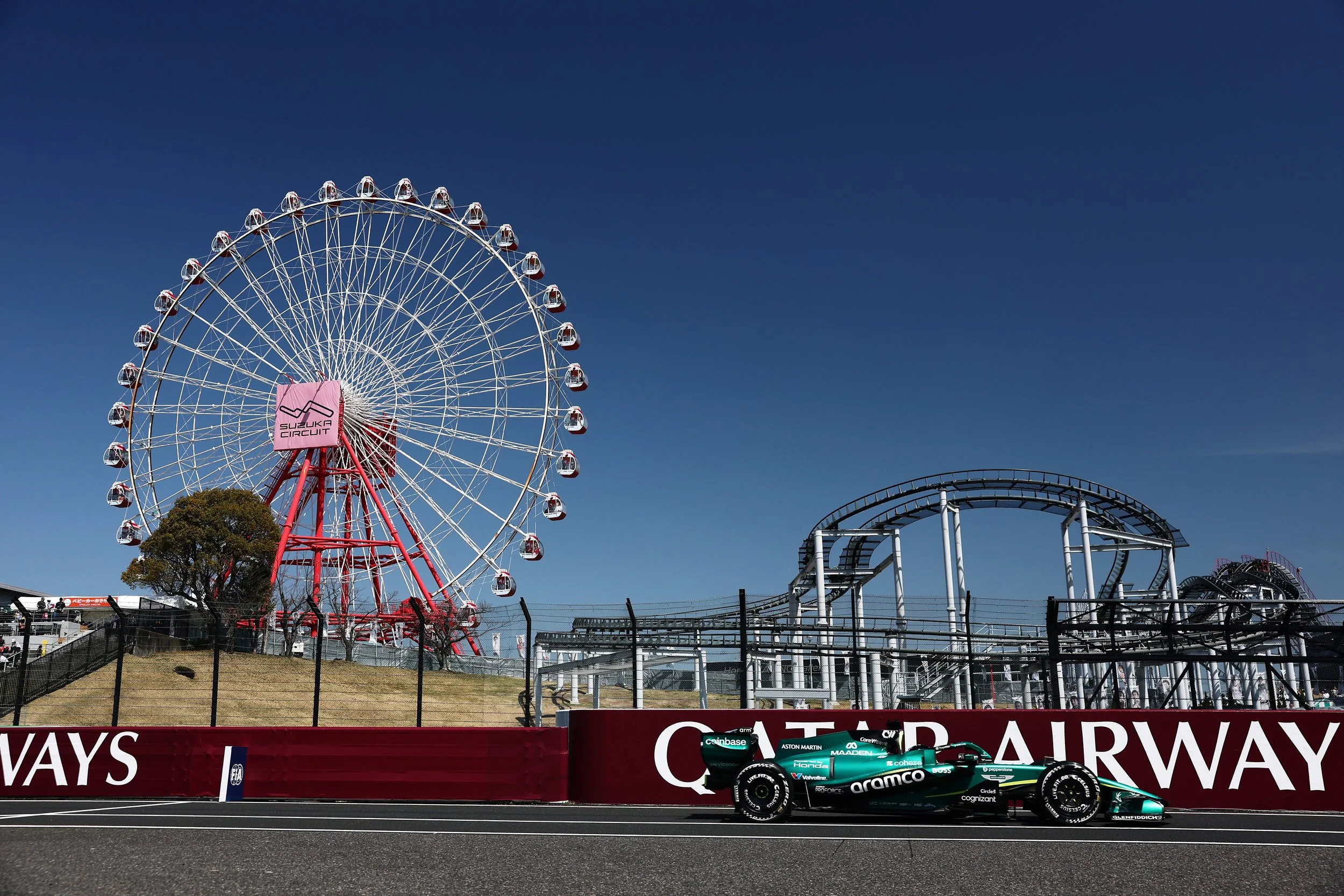 A Formula 1 race car on a racetrack with a Daytona International Speedway Ferris wheel in the background against a blue sky.