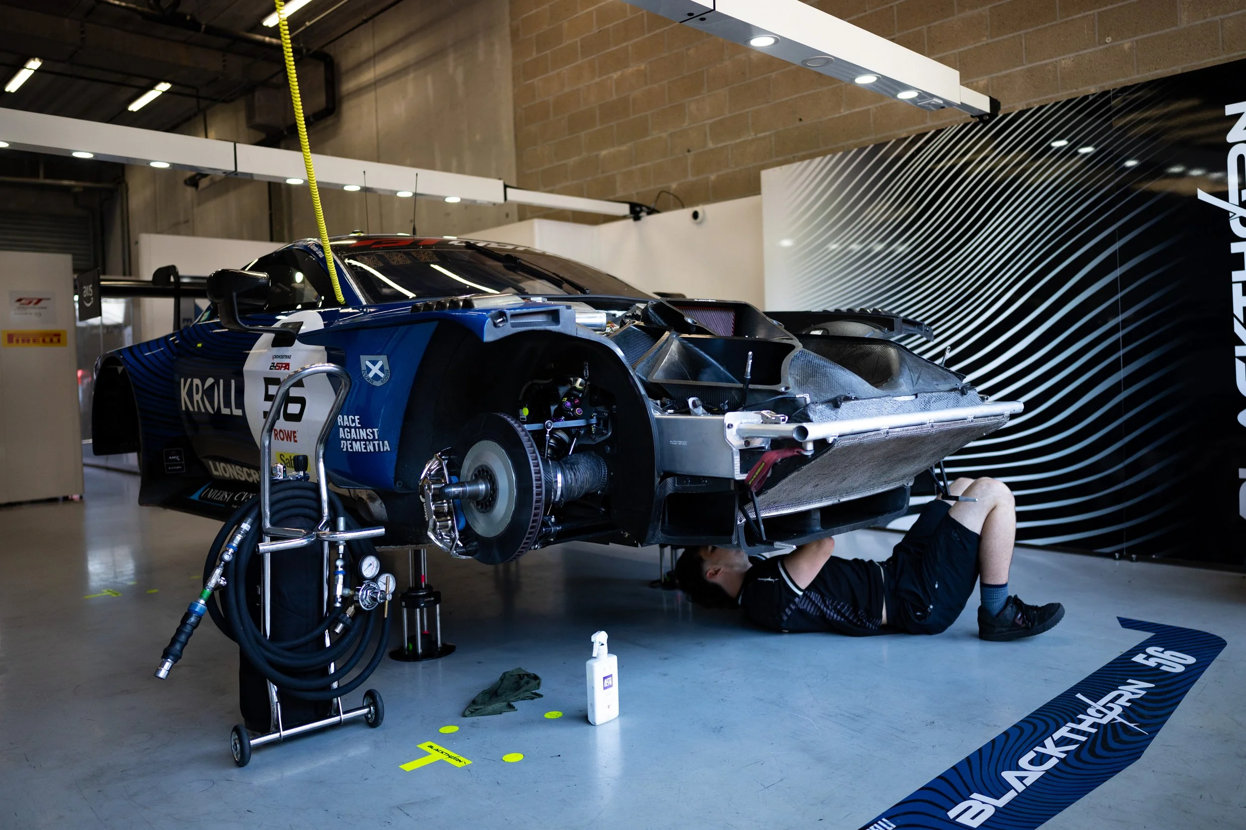 Race car on a lift in a garage with a mechanic working underneath it.