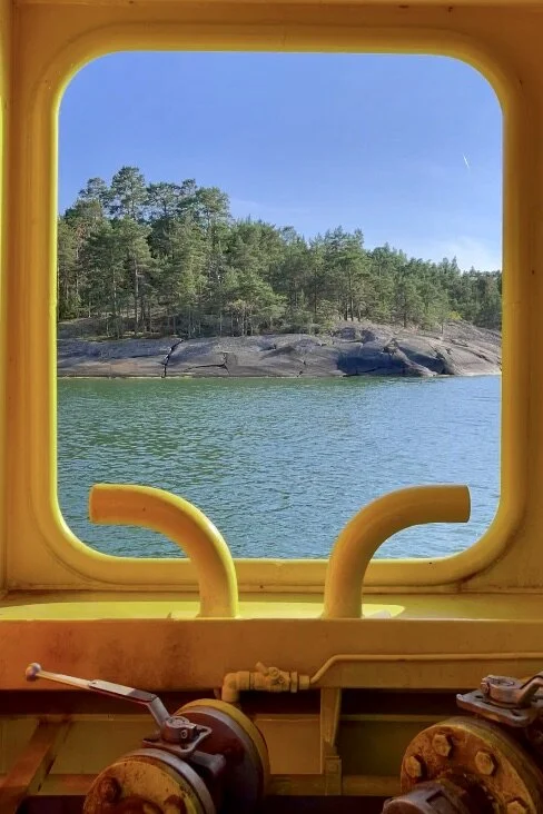 Keltaisen lautan ikkunasta näkyy merta, kalliota ja puita.