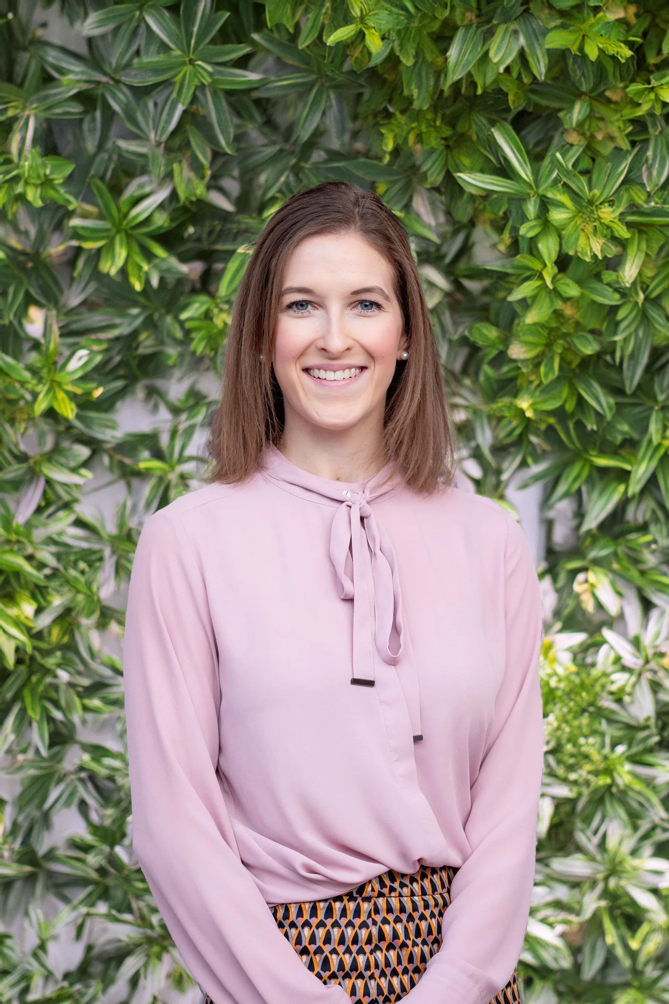 Jessica Valenzuela smiling in front of a wall of greenery