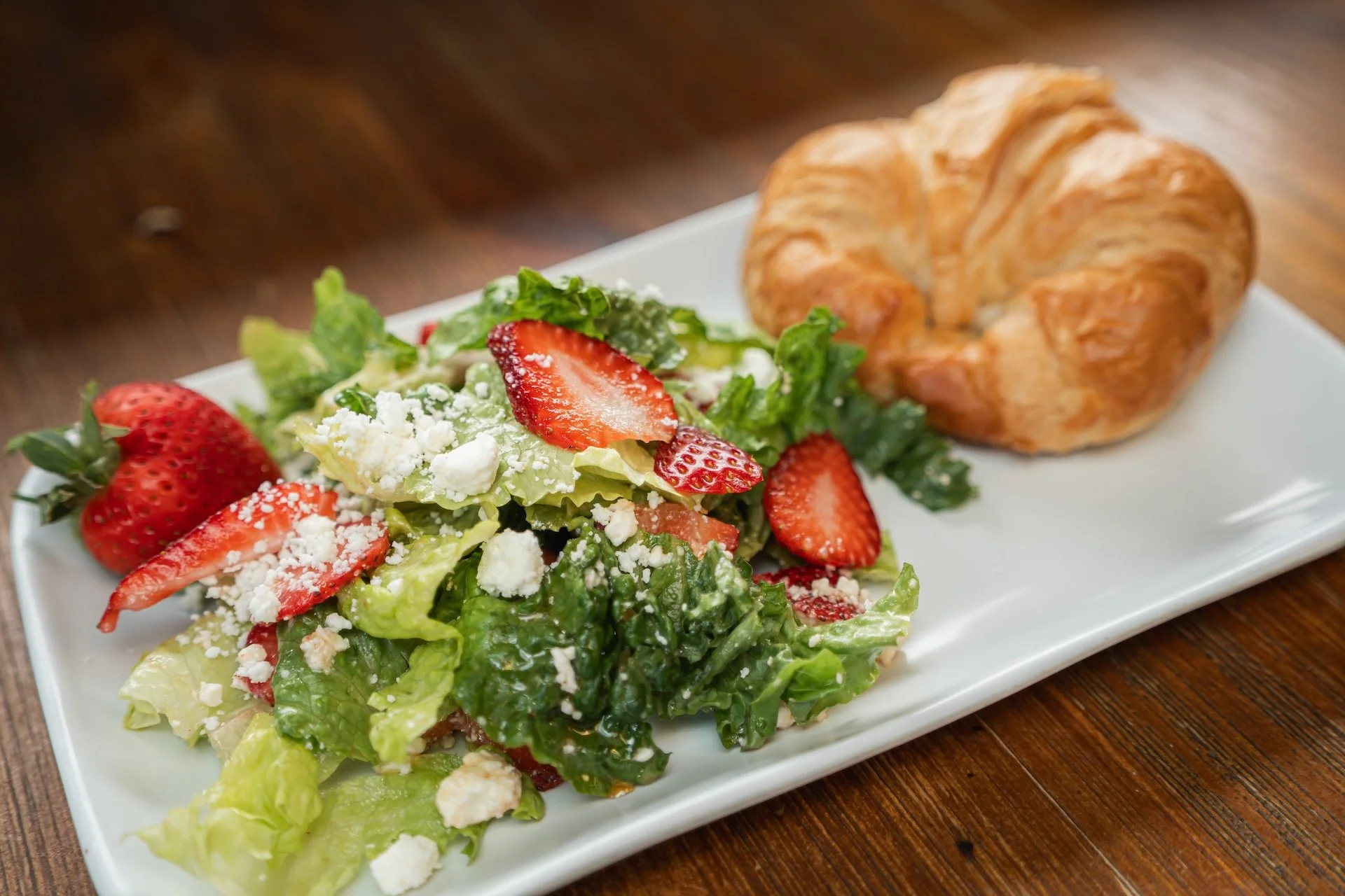 Fresh strawberry and cheese salad with croissant on a white plate.