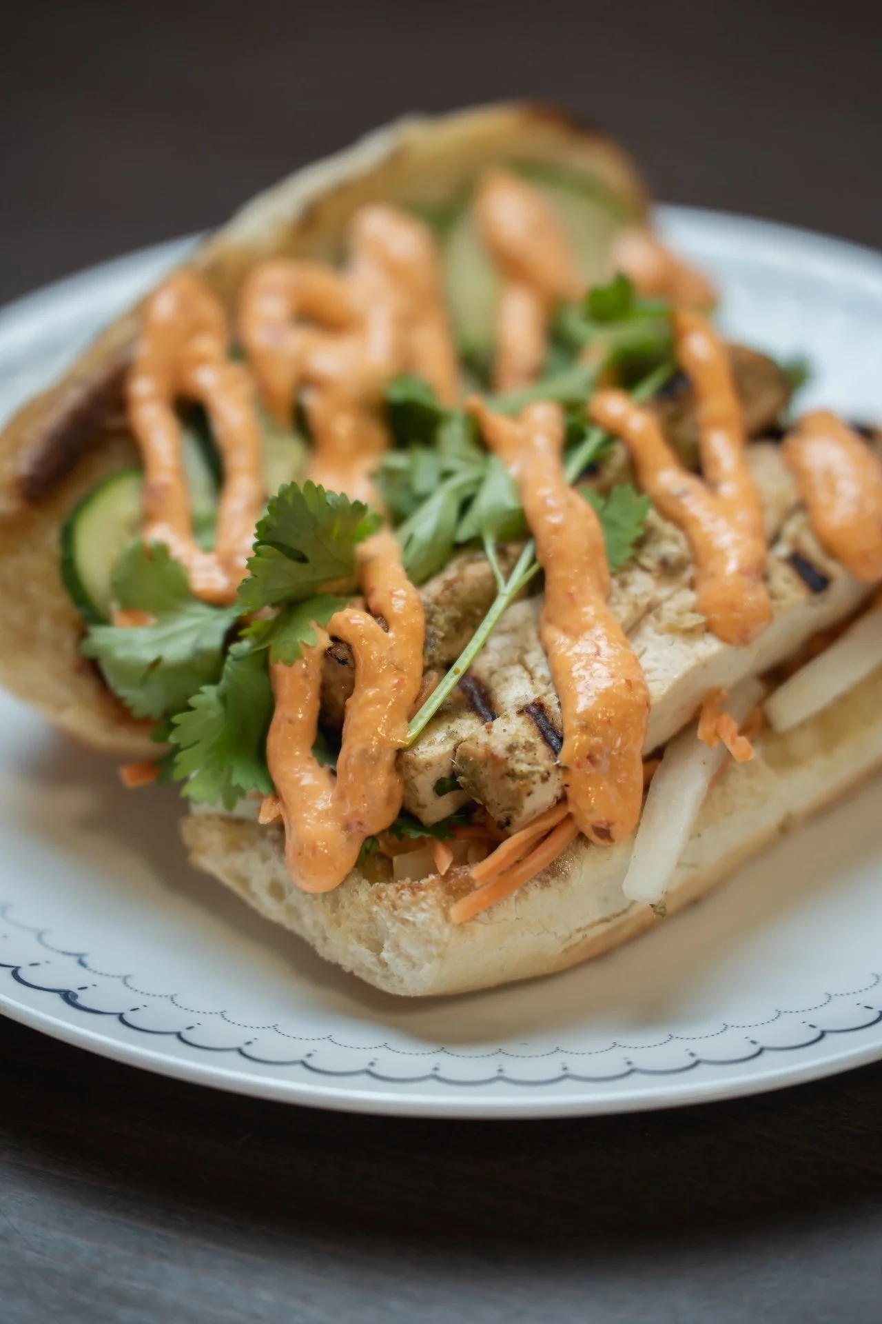Close-up of a kabob sandwich with grilled chicken, cucumbers, shredded carrots, cilantro, and sauce on a bun.