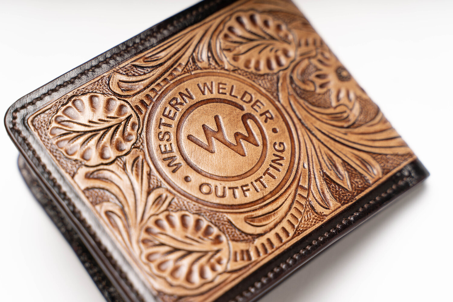 Close-up of a leather wallet with intricate floral engraving and "Western Welder Outfitting" logo.