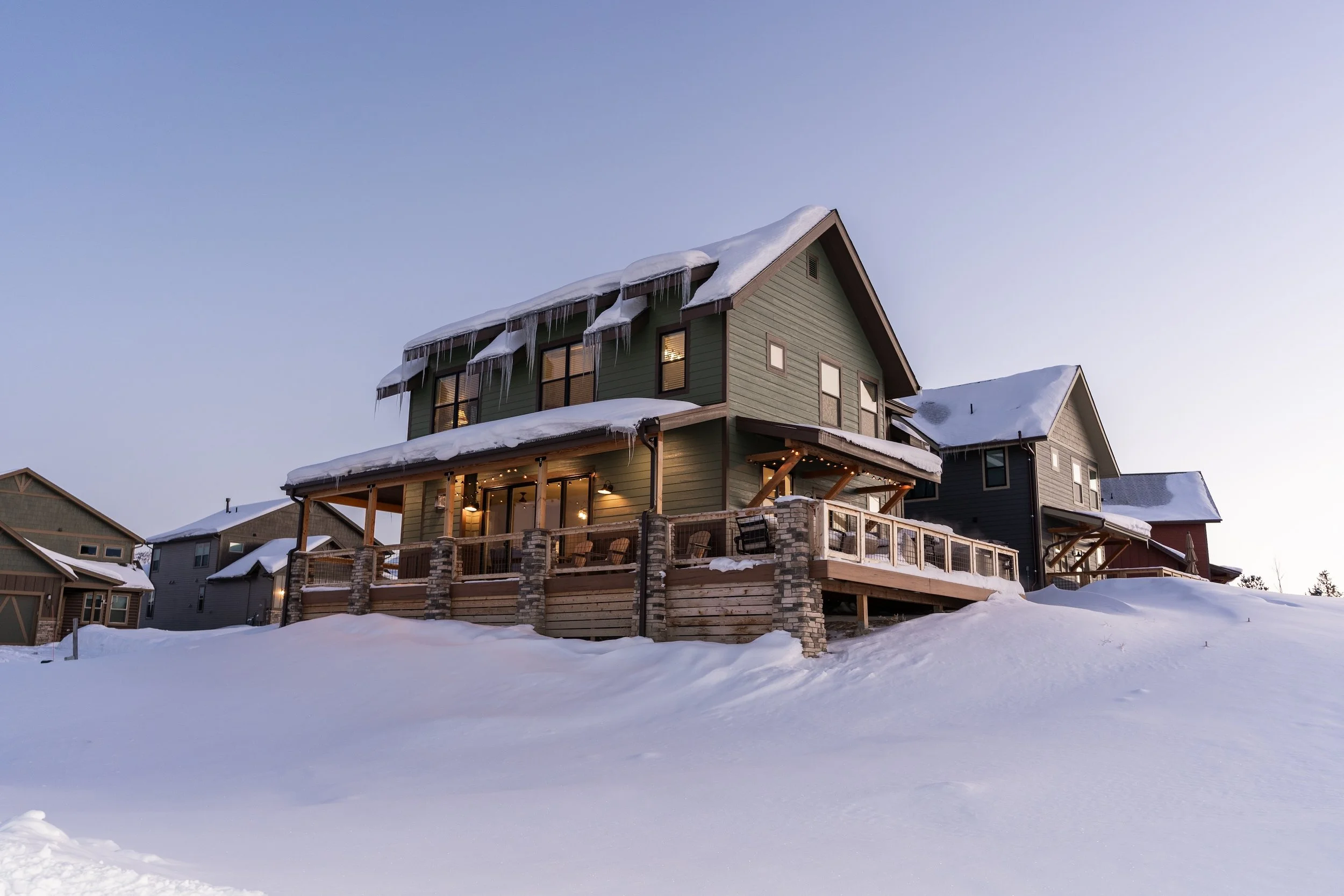 Snow-covered house with icicles hanging from the roof and lit windows, in Whitefish, Montana.