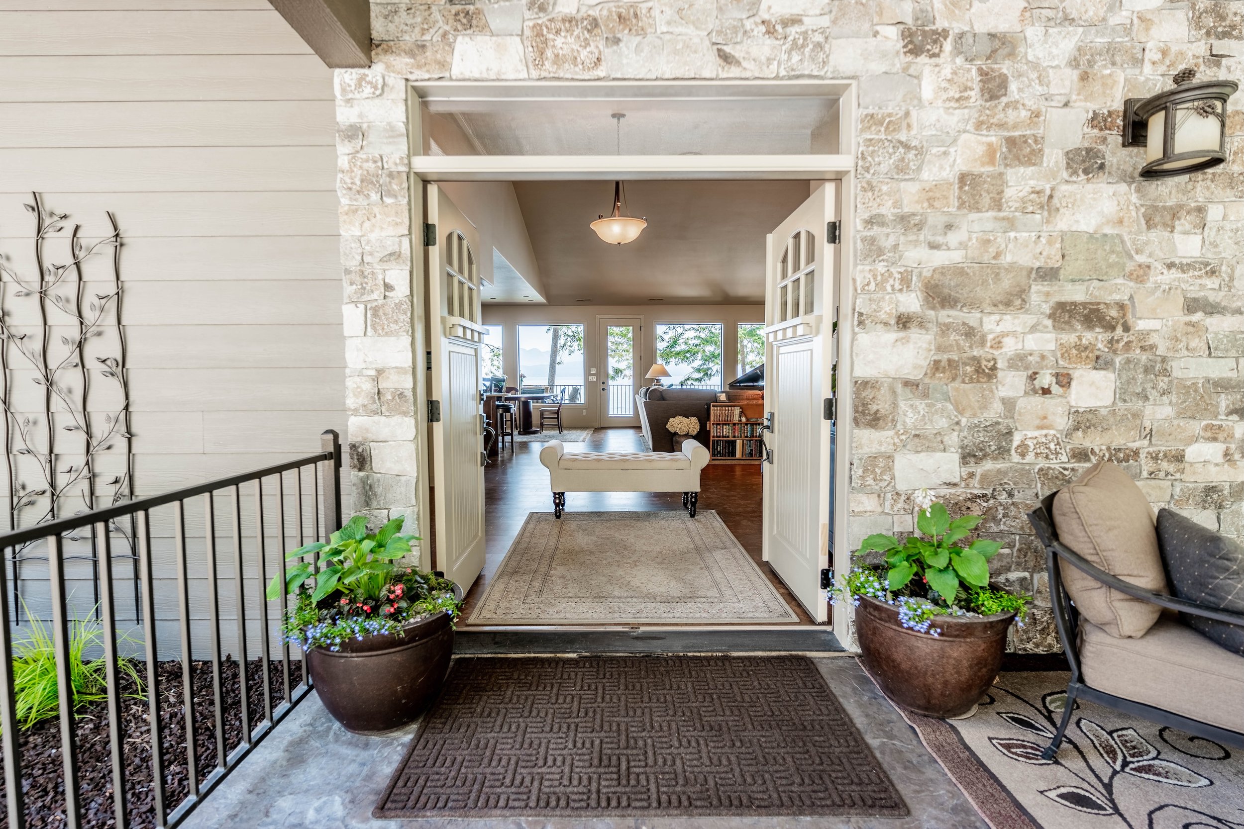 View from porch into interior living room with double doors, stone wall, plants, and furniture. Real Estate photographer based in Kalispell, Montana and the Flathead Valley.