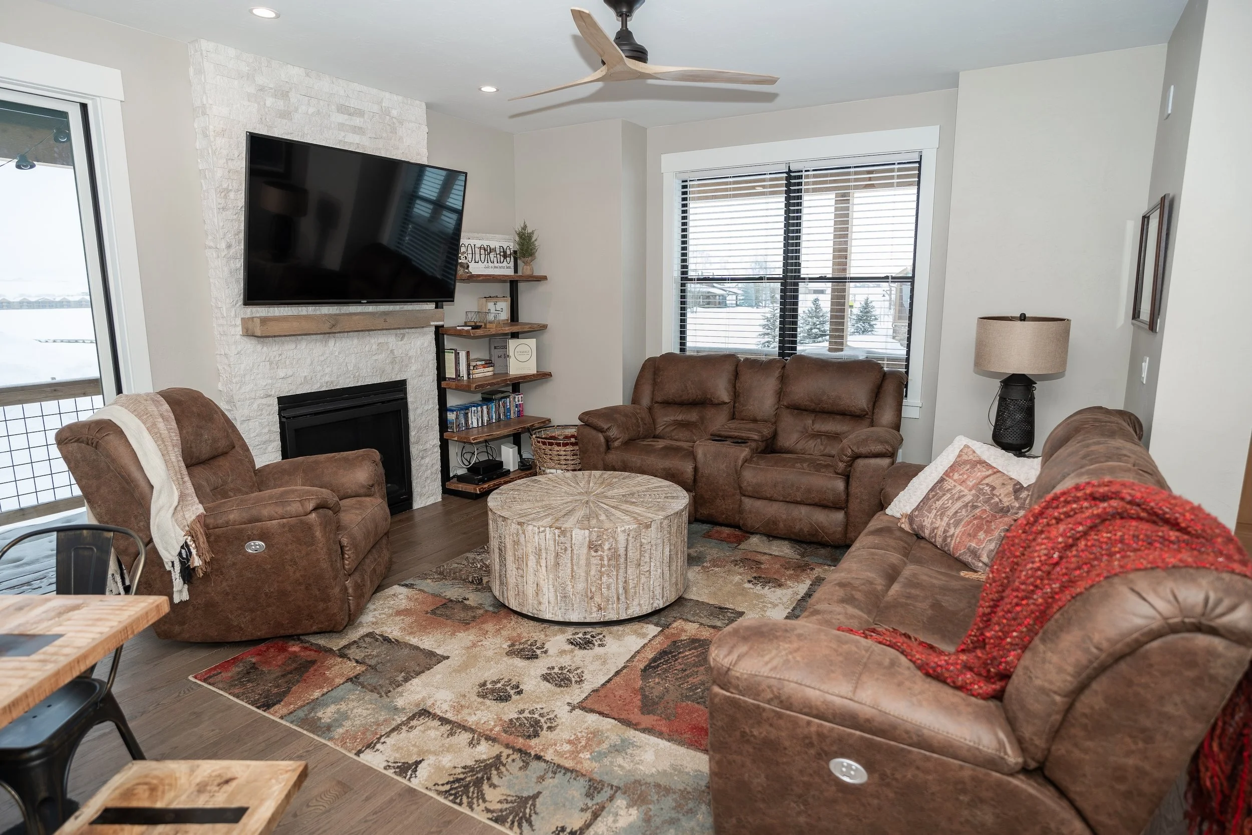 Living room with brown leather sofas, a large TV mounted above a rustic white fireplace, a wooden coffee table, Real Estate photographer based in Kalispell, Montana and the Flathead Valley.