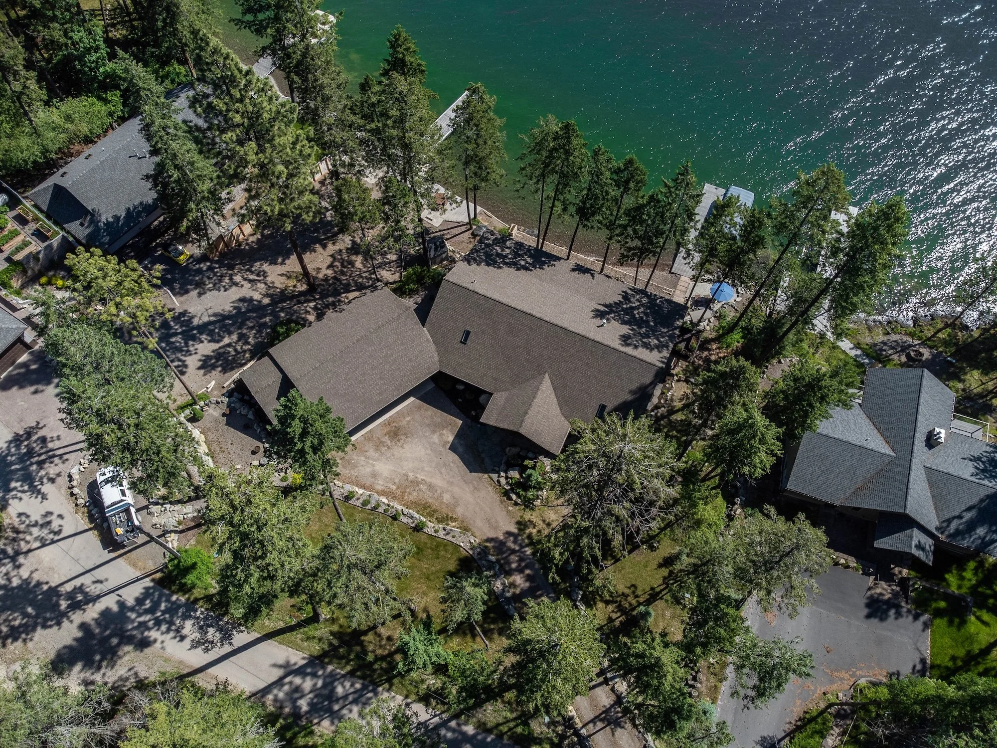Aerial view of houses and trees along a lake shoreline, with a driveway and parked truck visible. Real Estate photographer based in Kalispell, Montana and the Flathead Valley.