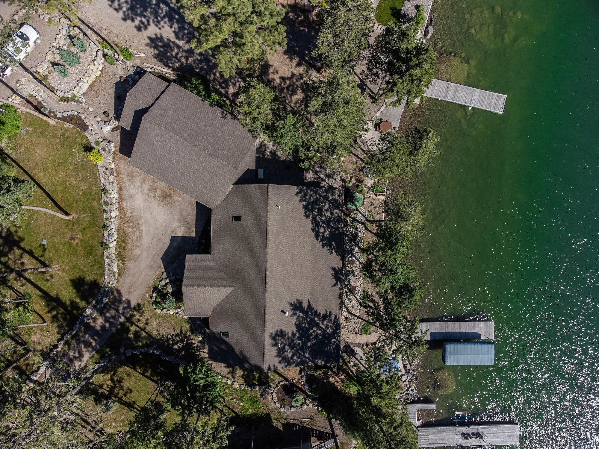 An aerial view of a lakeside property with a house, dock, boat lift, shoreline, and surrounding trees. Real Estate photographer based in Kalispell, Montana and the Flathead Valley.