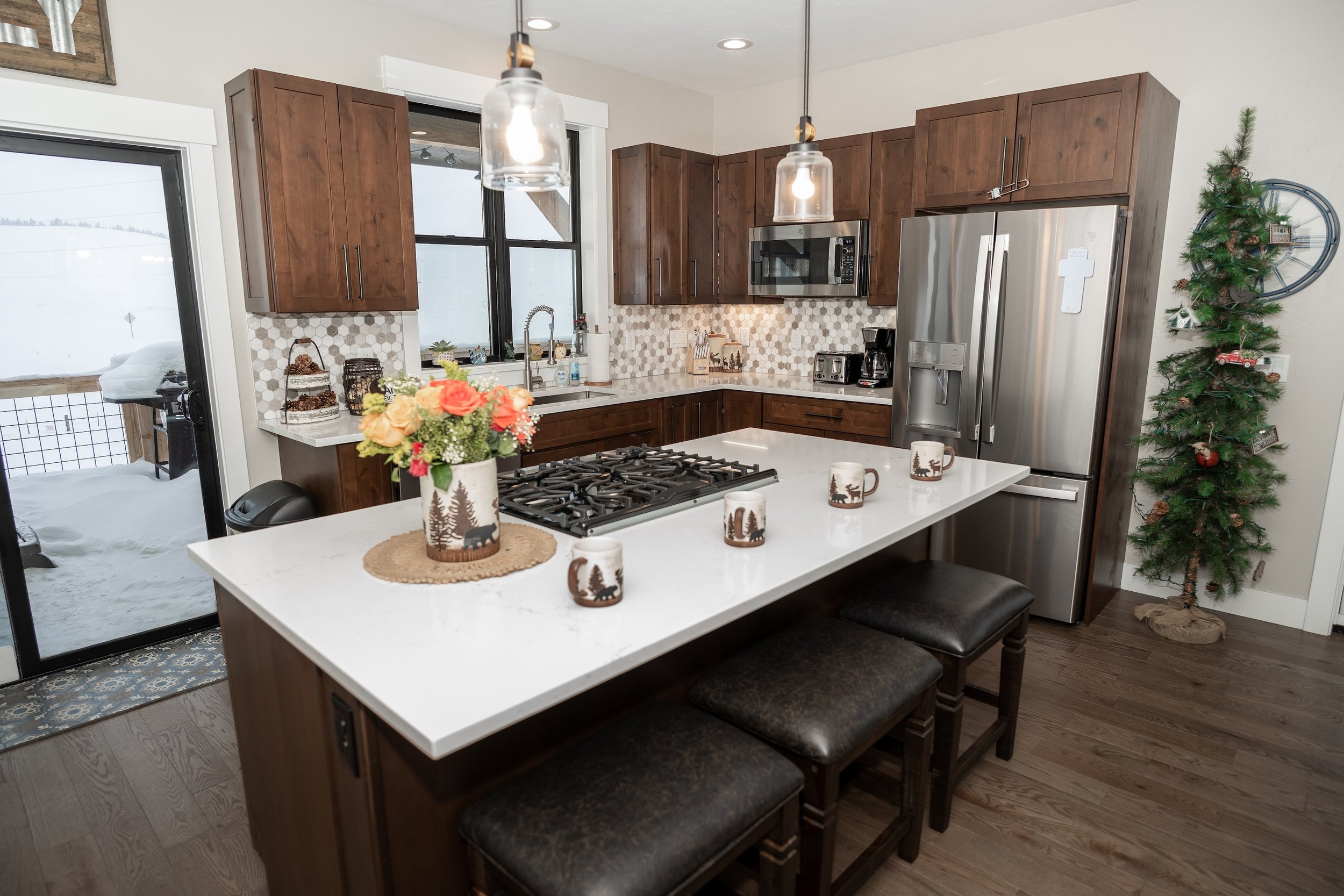 Modern kitchen with white island, brown wooden cabinets, stainless steel appliances, and a small Christmas tree in the corner. Real Estate photographer based in Kalispell, Montana and the Flathead Valley.