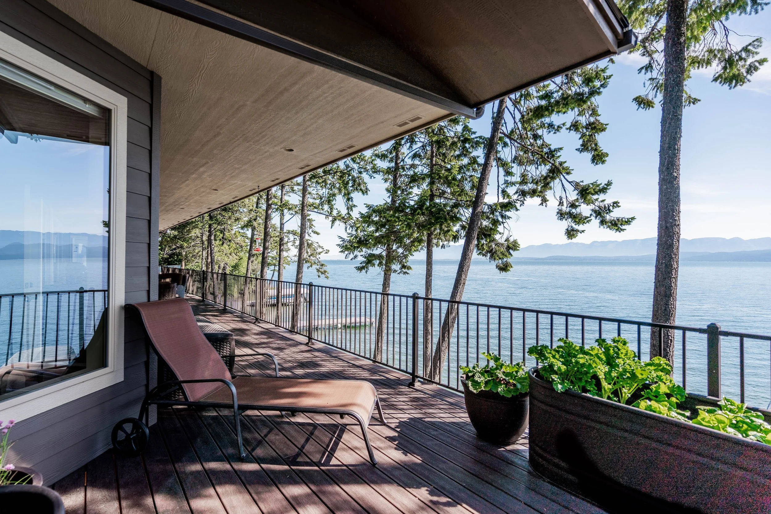 A balcony with a lounge chair overlooking a lake with trees and distant mountains. Real Estate photographer based in Kalispell, Montana and the Flathead Valley.