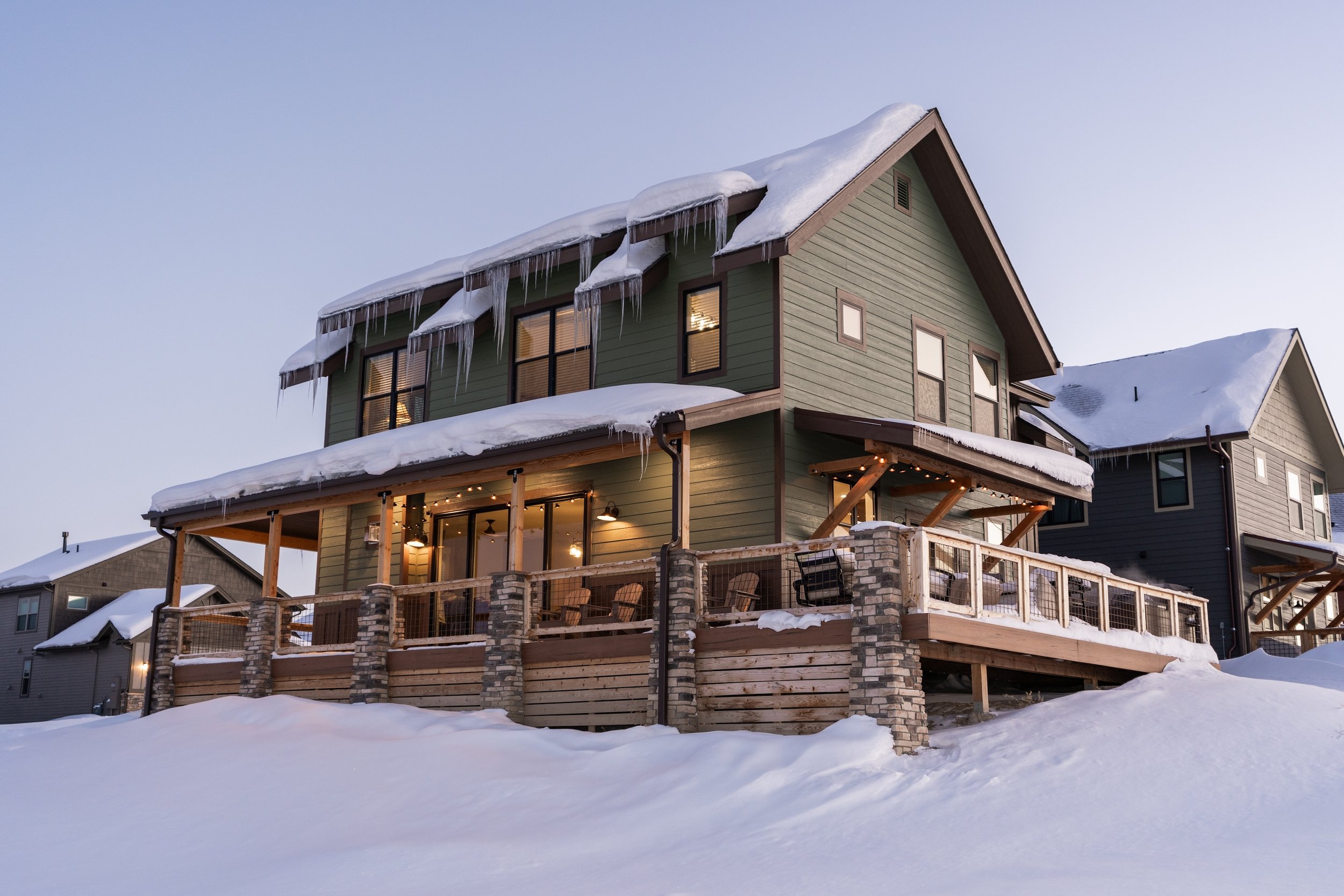 A two-story house with green siding and a large wooden deck. Real Estate photographer based in Kalispell, Montana and the Flathead Valley.