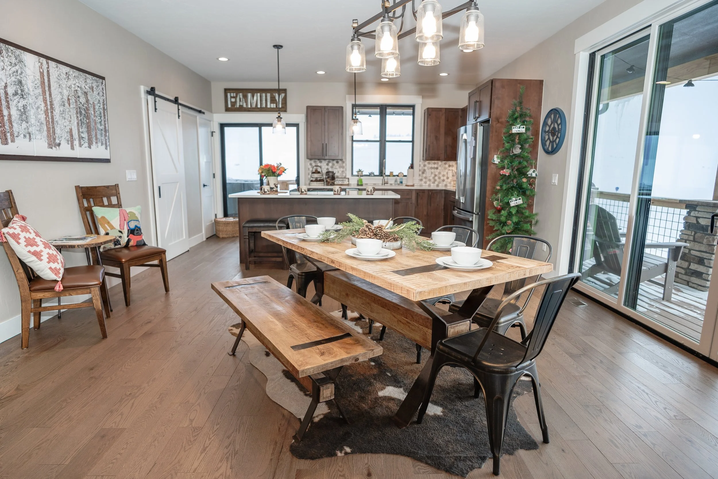 Open-concept kitchen and dining area with a wooden table set for six, a bench, metal chairs, wooden flooring, Real Estate photographer based in Kalispell, Montana and the Flathead Valley.