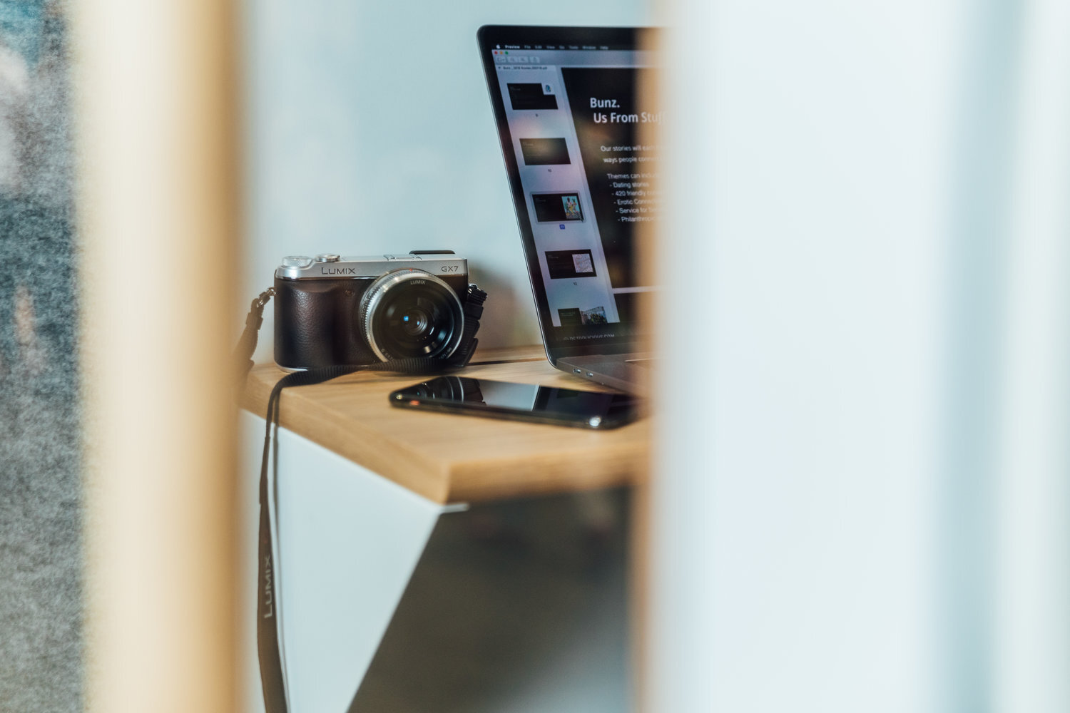 Camera and laptop on a wooden desk with a smartphone.