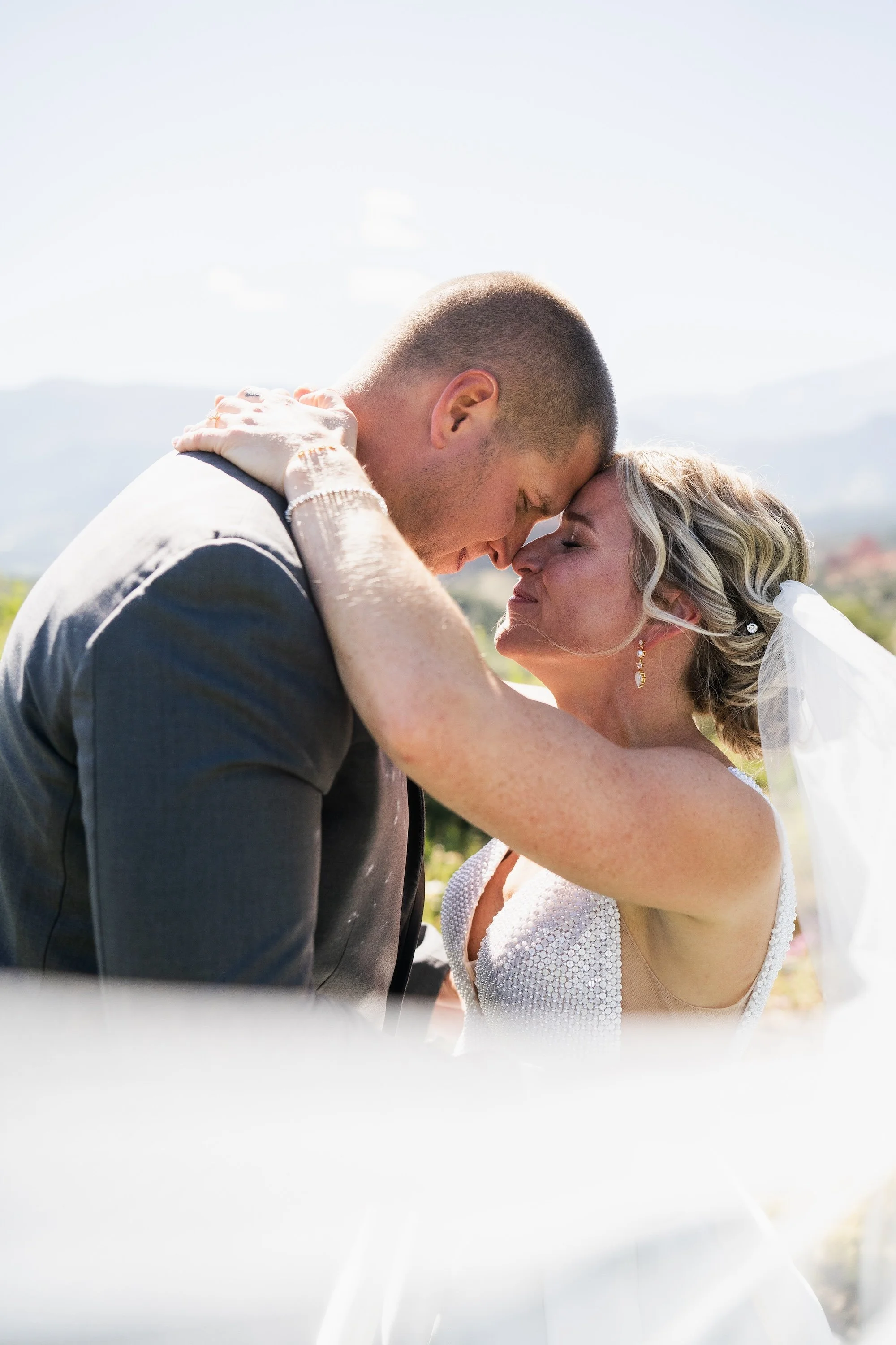Bride and groom embracing closely, with eyes closed, in a romantic outdoor setting.