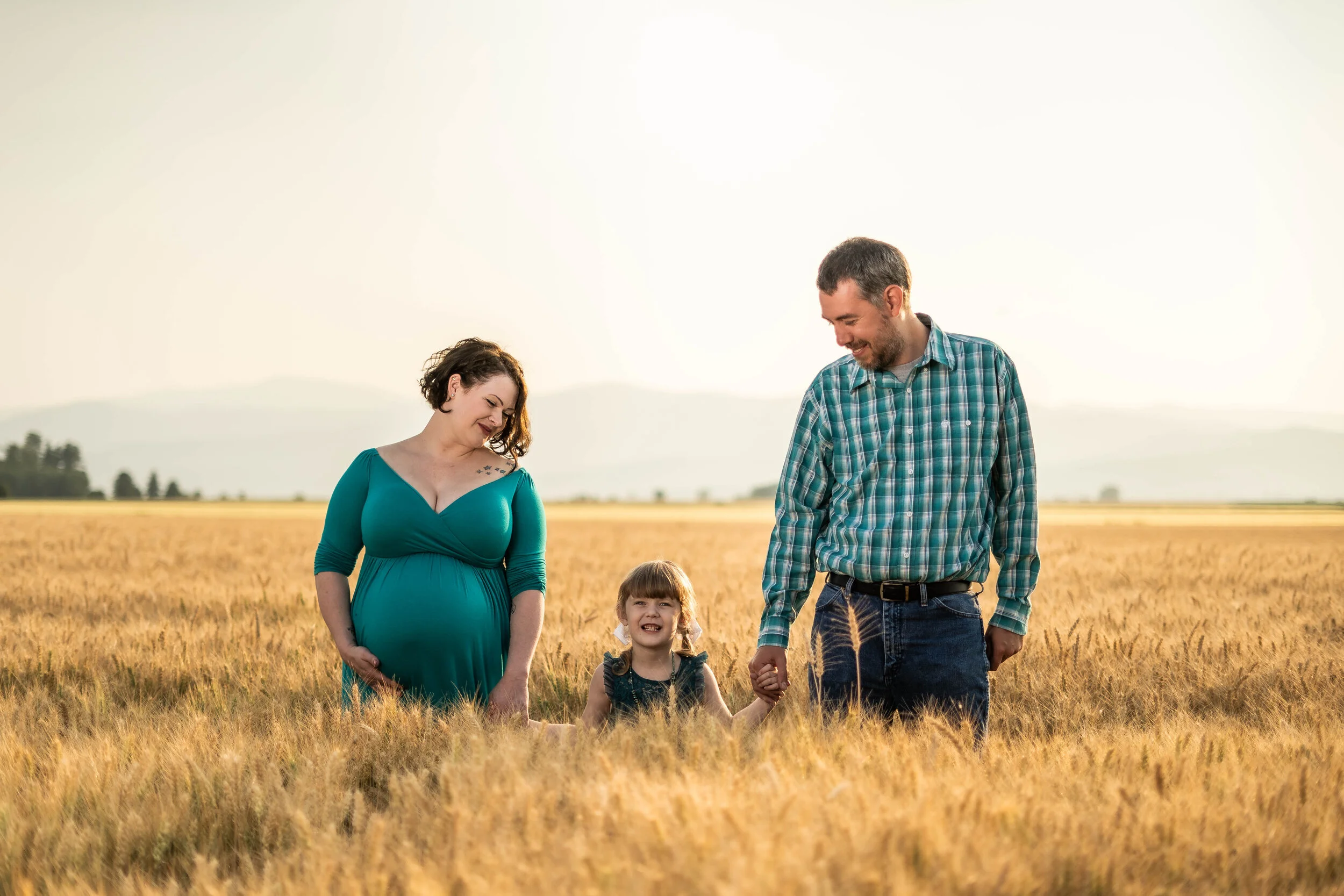 A pregnant woman, a little girl, and a man walking in a field of wheat, smiling and holding hands.