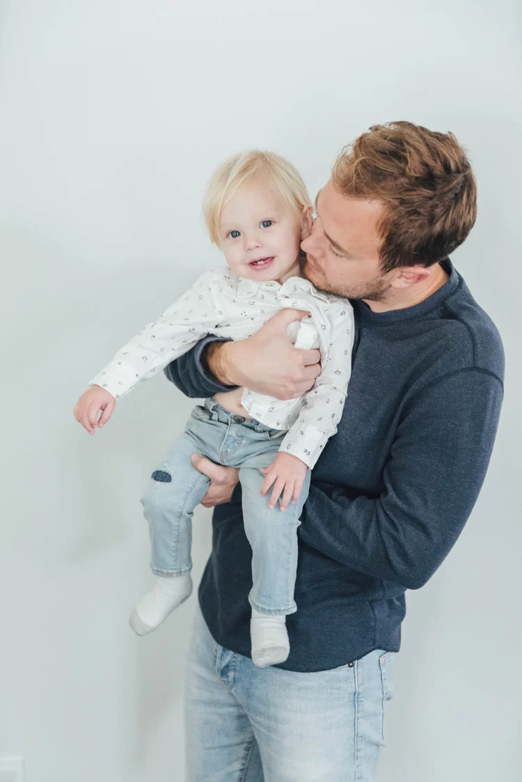 Man holding a smiling baby wearing a white shirt and light jeans