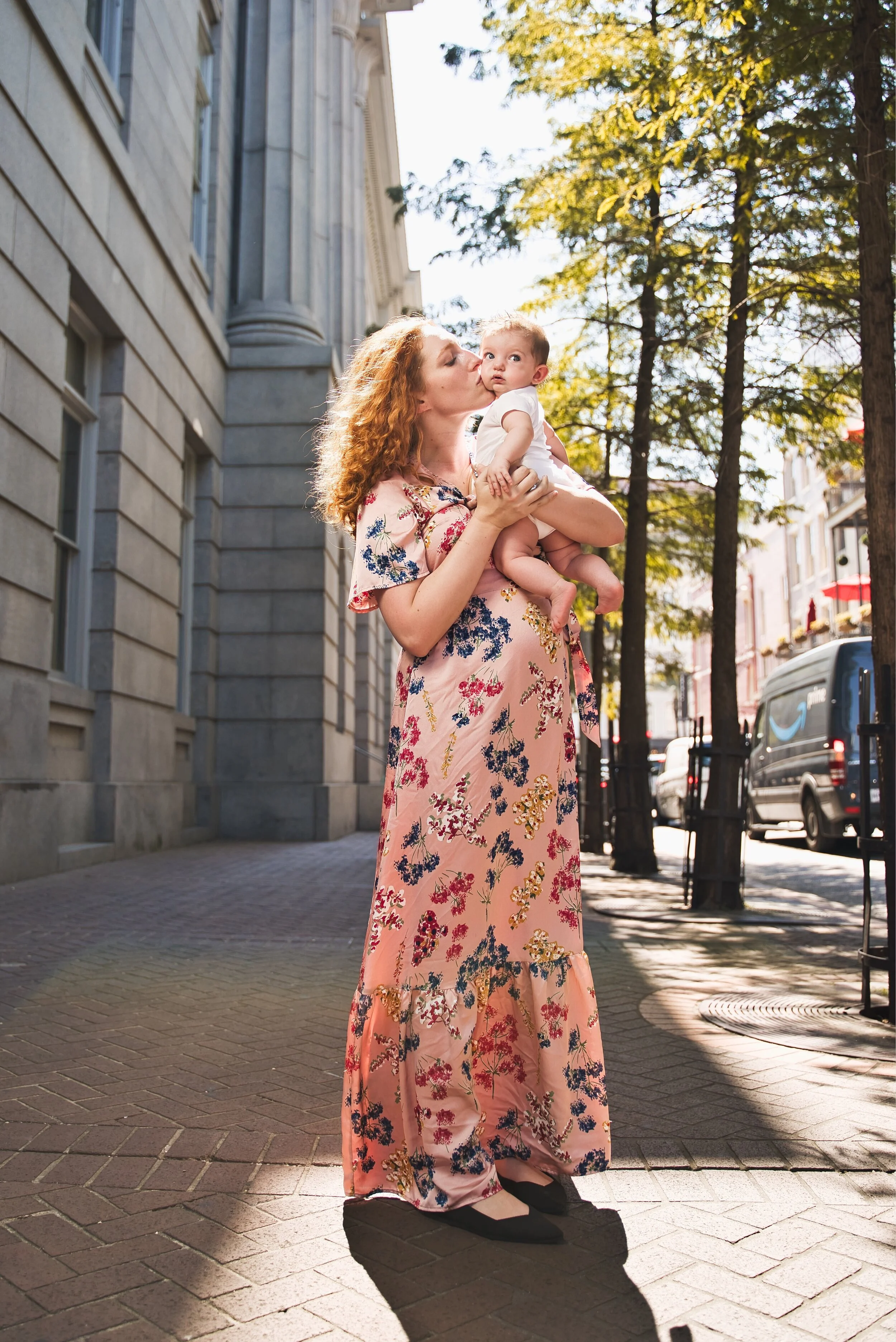 Woman in floral dress holding baby on urban street.