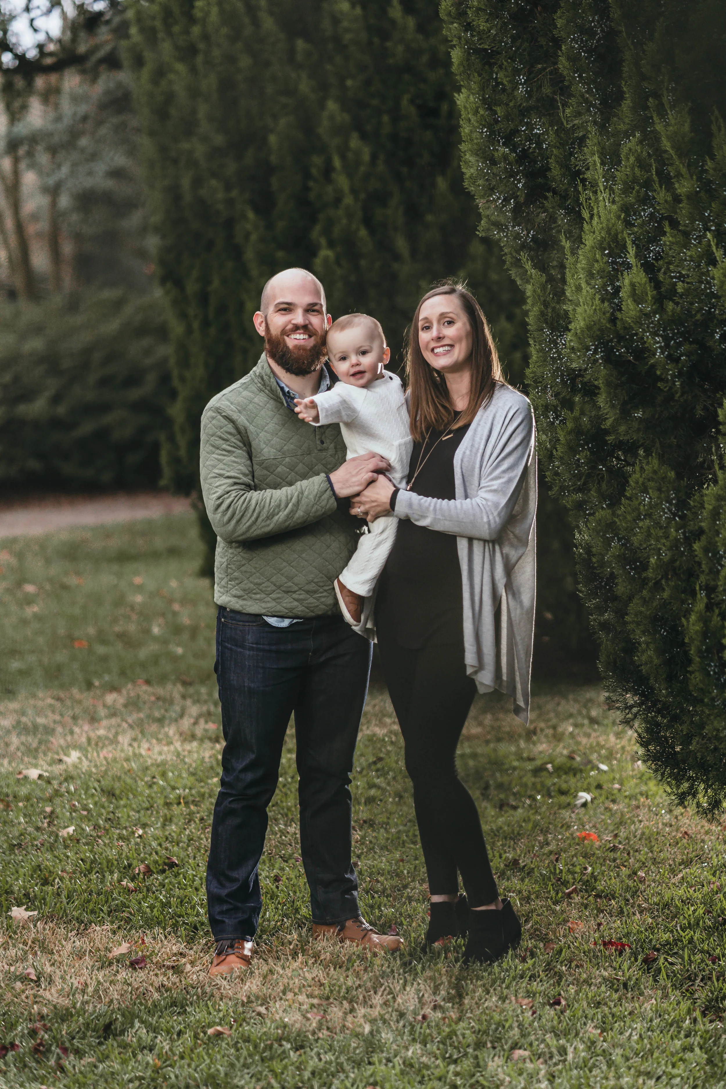 Family of three posing outdoors with greenery