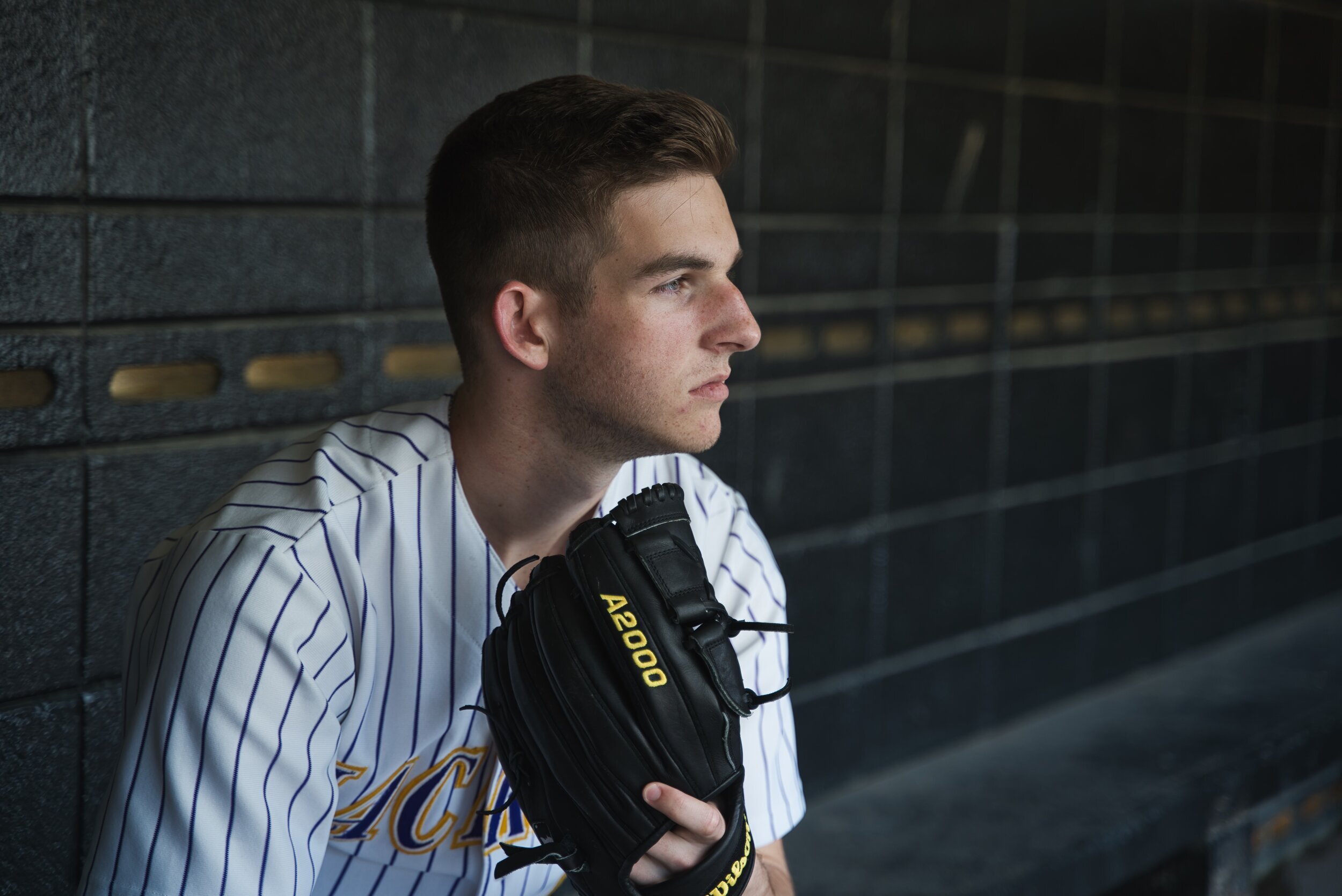 Baseball player in striped jersey holding black glove in dugout.