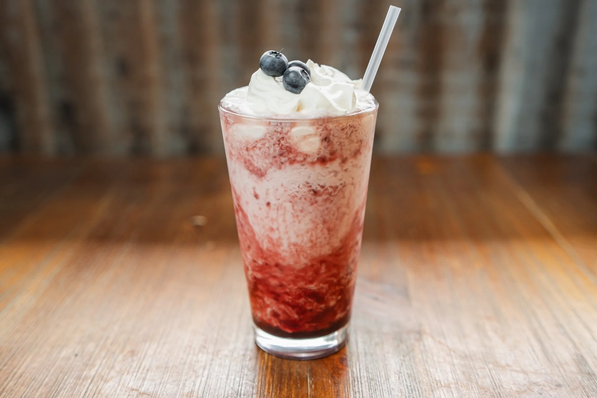 A tall glass of strawberry blueberry smoothie topped with whipped cream and blueberries, with a straw.