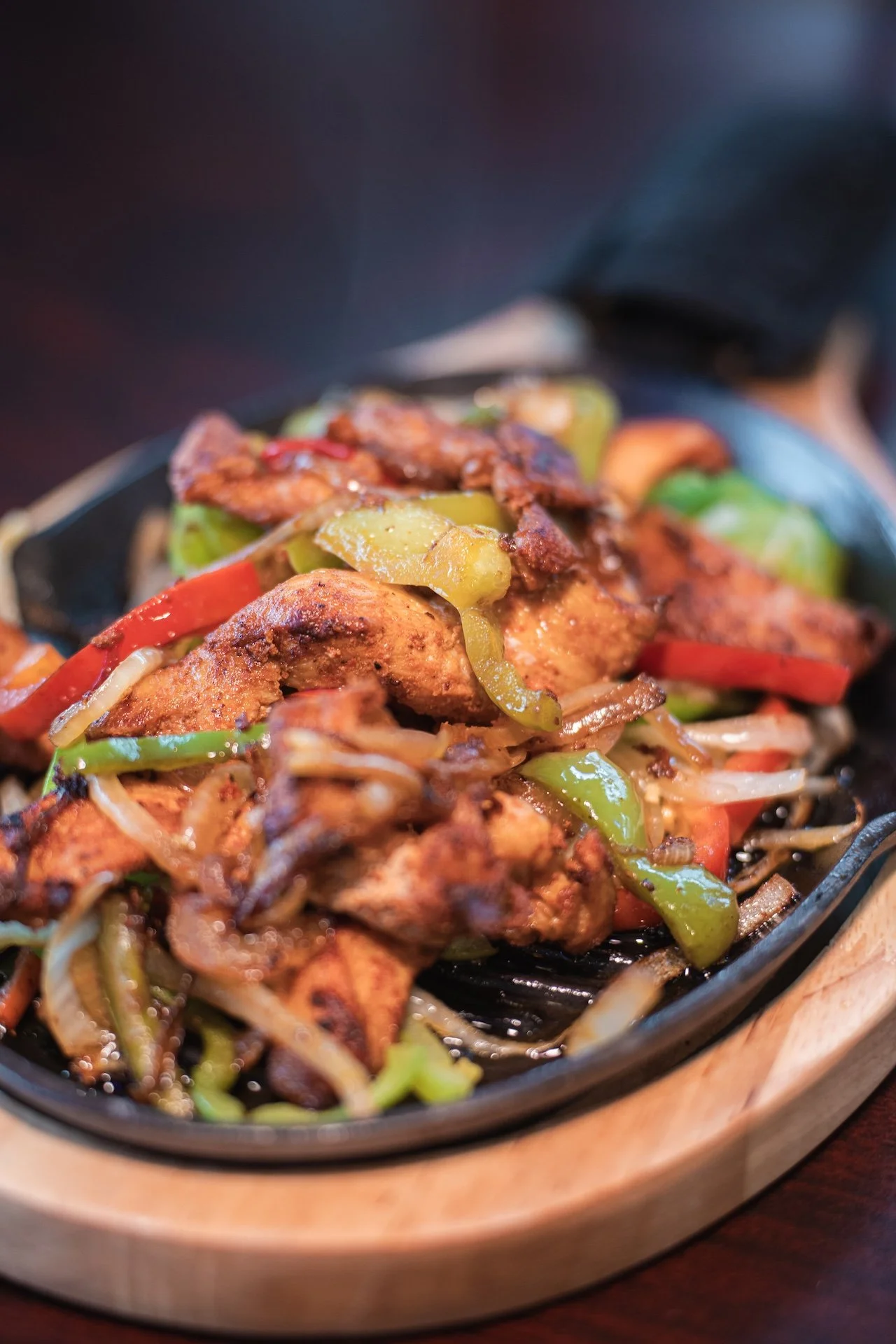 Cooked chicken and vegetable stir-fry on a sizzling plate with bell peppers and onions.