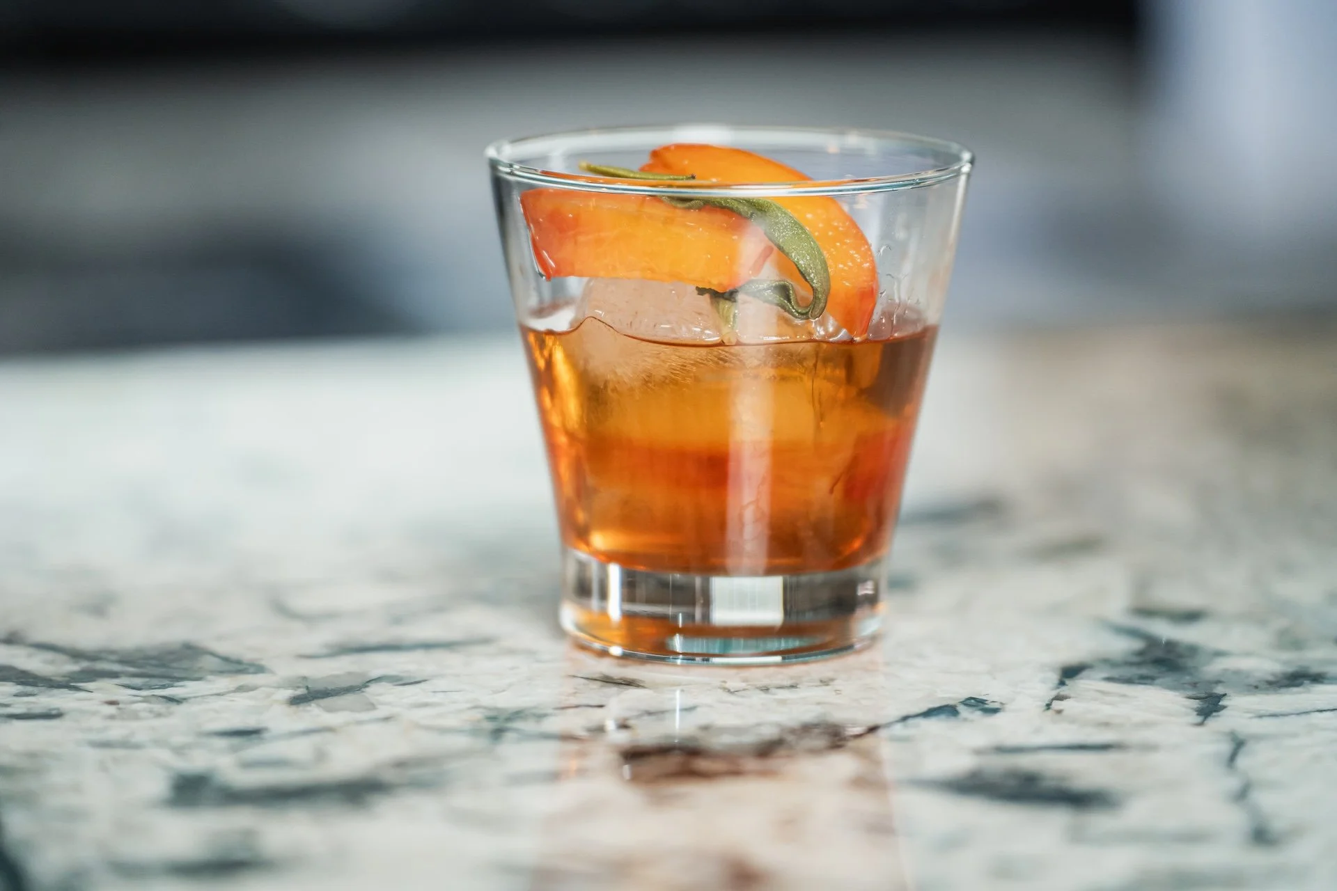 A glass of iced tea with an orange slice and a green lemon peel garnish on a marble surface.