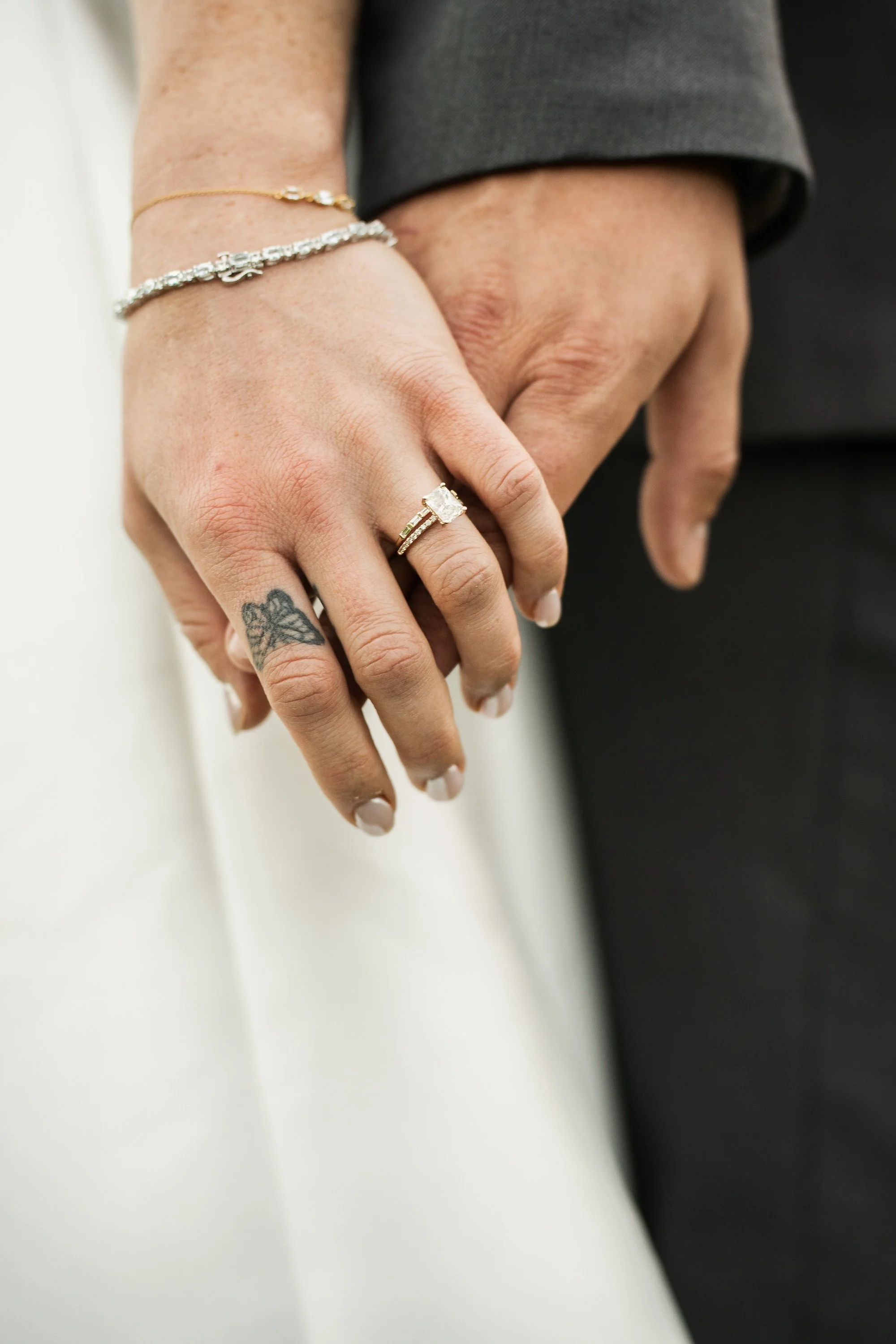 Close-up of a couple holding hands, focusing on wedding rings and a tattoo on the bride's hand.