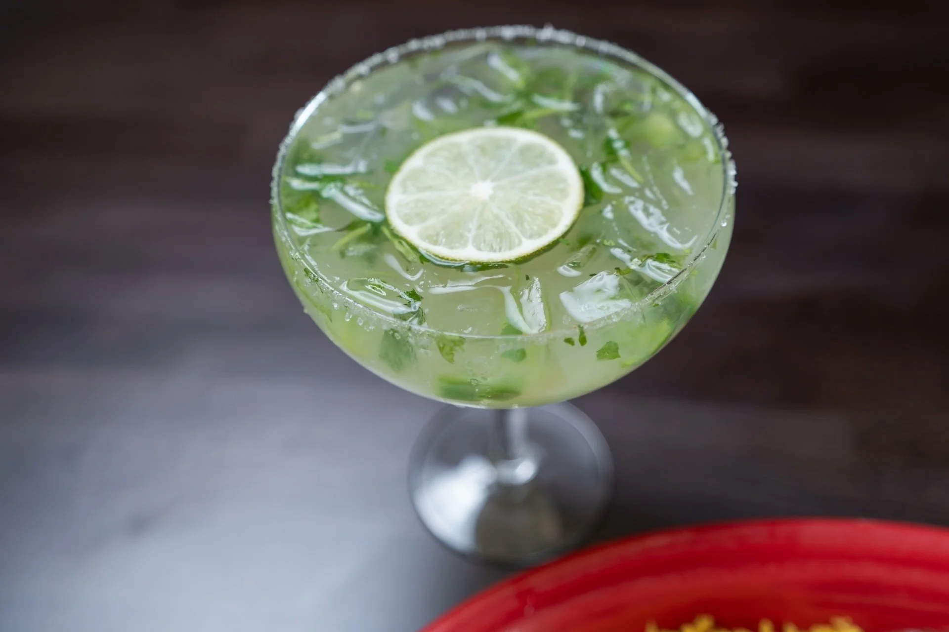 A glass of limeade with ice and a slice of lime on top, placed on a dark wooden surface.