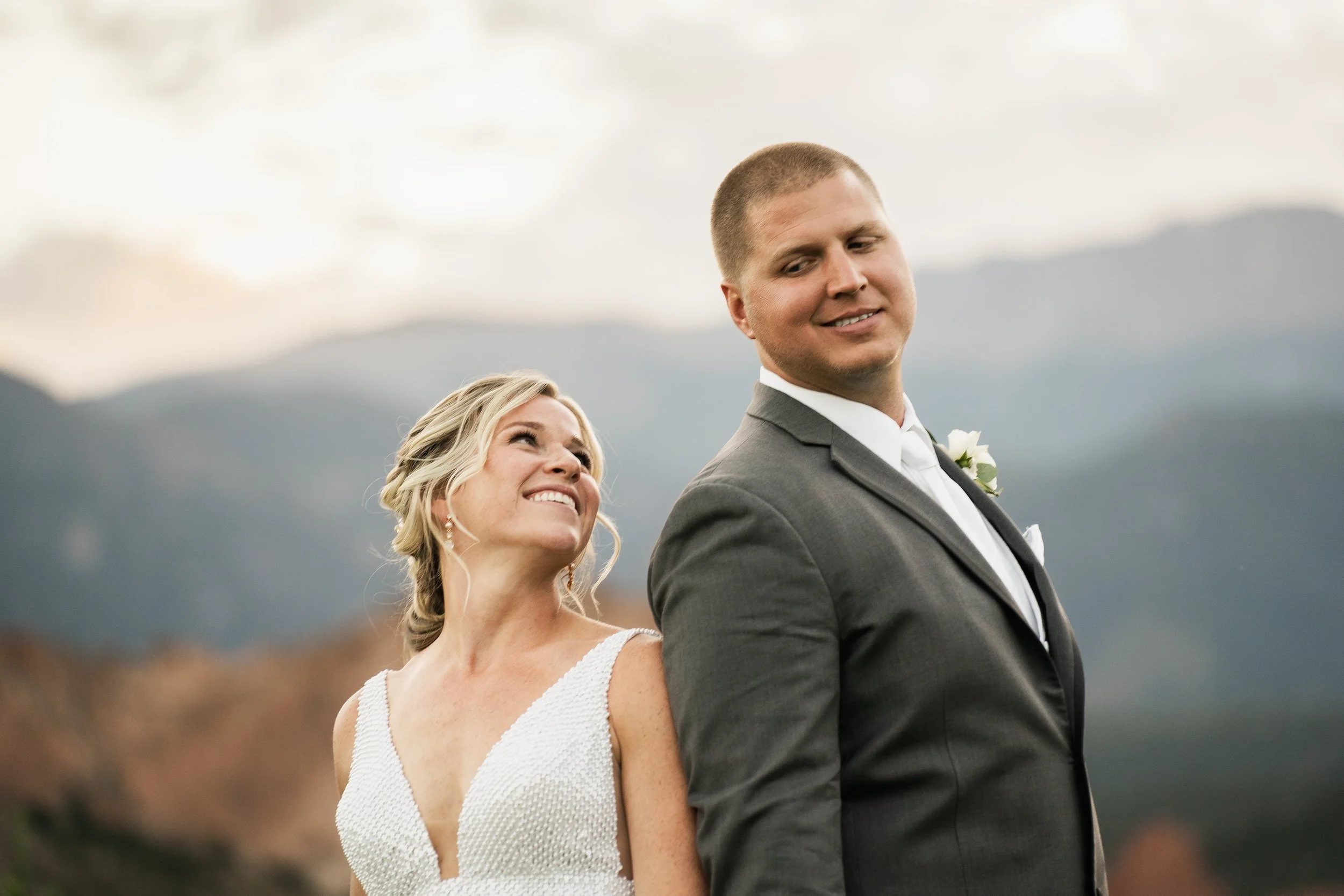Bride and groom smiling in outdoor setting with mountain backdrop.
