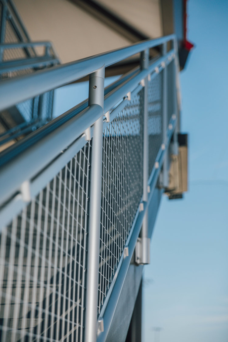 Close-up of a modern metal railing with mesh fencing, outdoor setting, blue sky background.