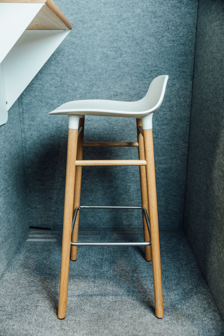 Modern white bar stool with wooden legs against gray background.