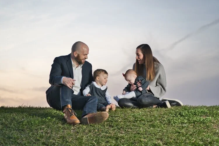 A family of four sitting on a grassy hill at sunset.