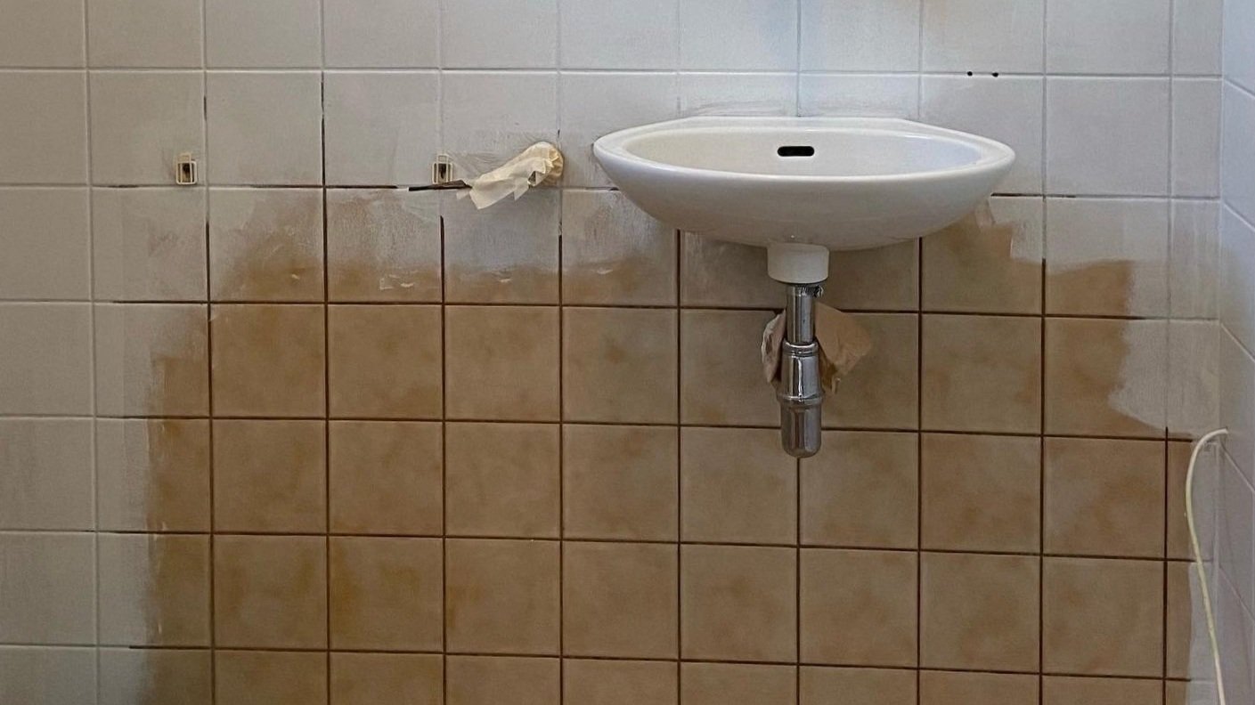 Old bathroom sink with discolored and partially painted tiles