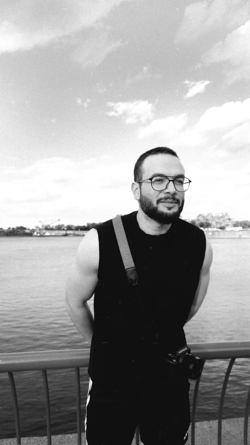 Djassem Haddad outdoors by the water, holding a camera