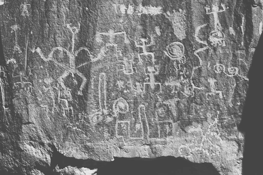 Ancient petroglyphs with intricate shapes and symbols on a rough rock surface.