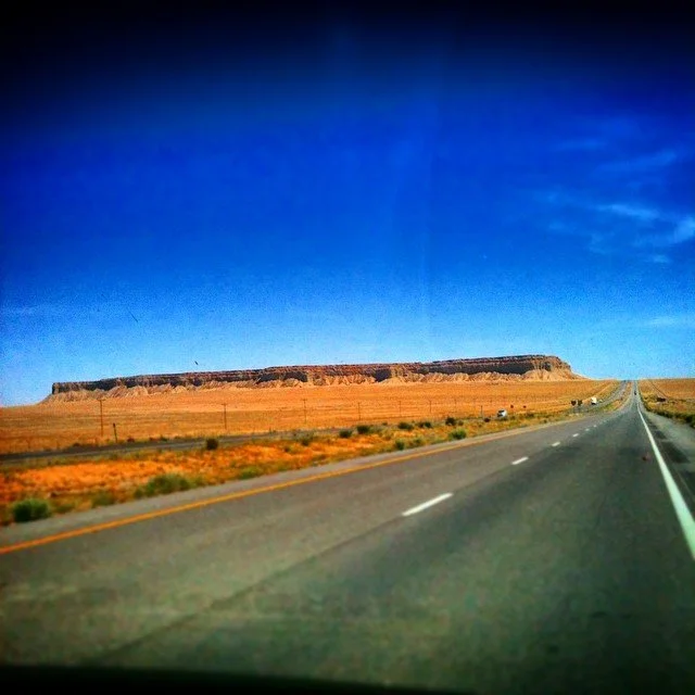 Open desert highway with flat-topped mesa under a bright blue sky