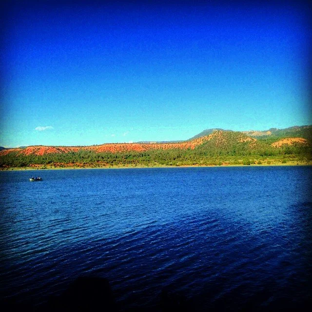 Serene lake with distant hills, under a clear blue sky.