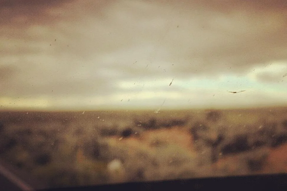 Cloudy sky over a blurred landscape seen through a dirty window.