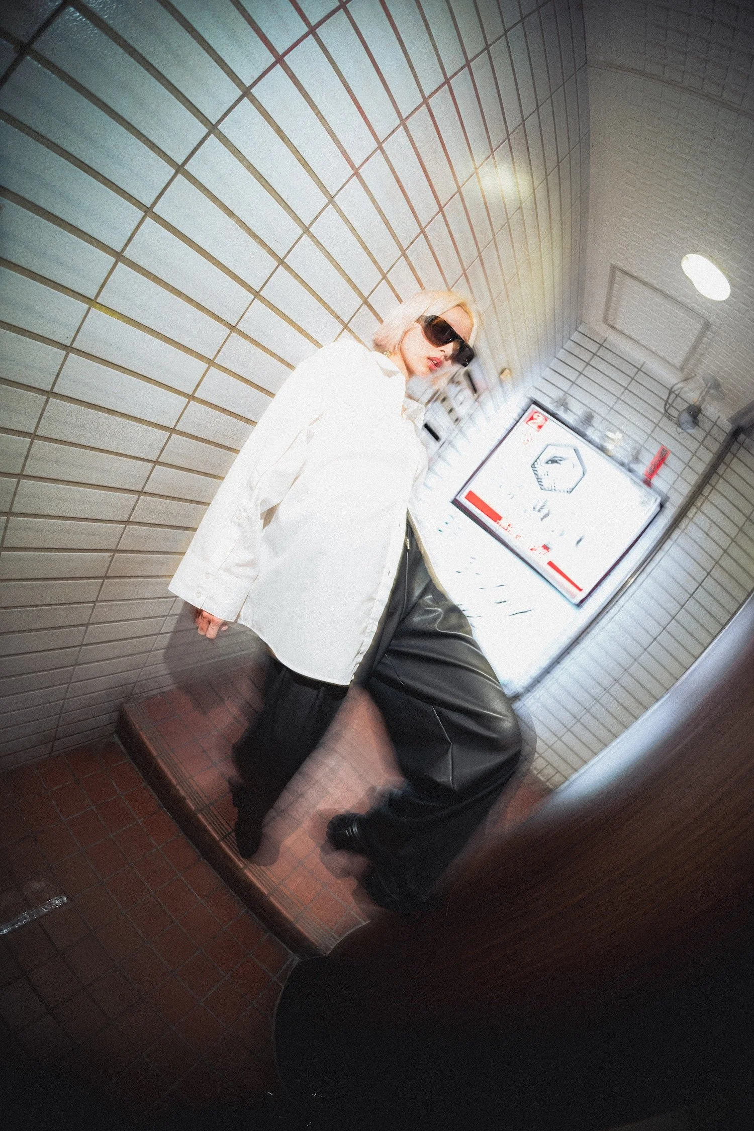 Fashion portrait of a model wearing Vasuma Eyewear sunglasses in Tokyo, photographed with a wide-angle lens inside an urban stairwell with creative motion effects. 