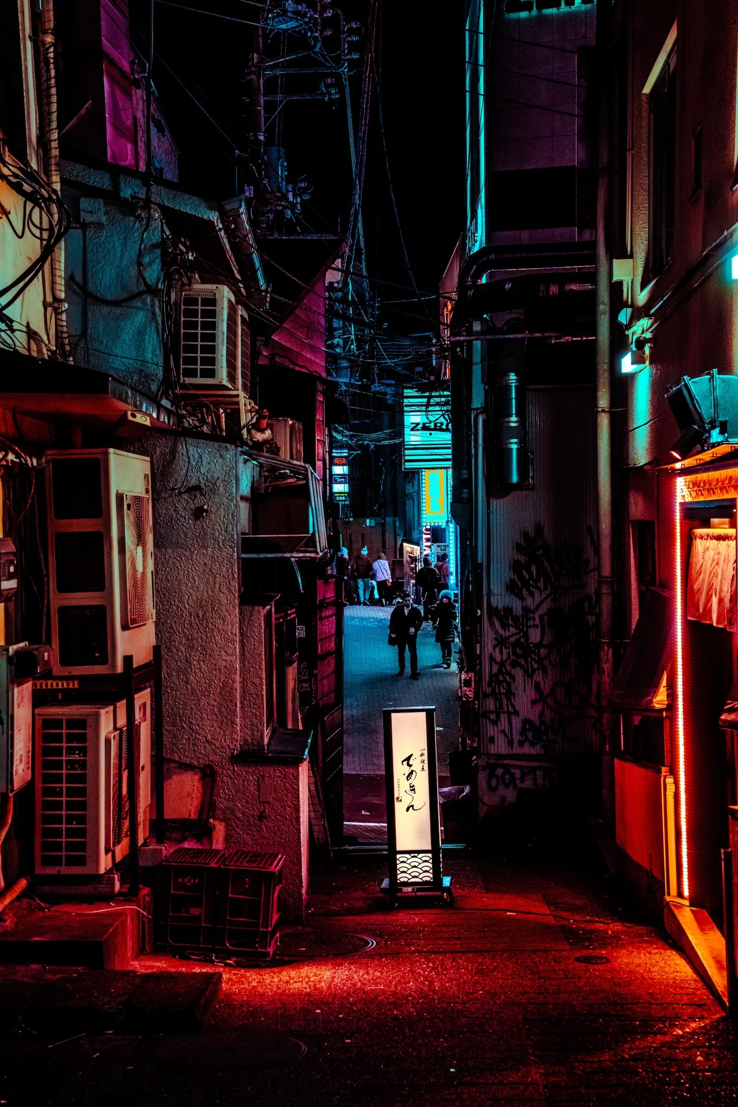 A narrow alley at night illuminated by neon and LED lights, with people walking in the distance, various signs, and exposed pipes and wires along the buildings.