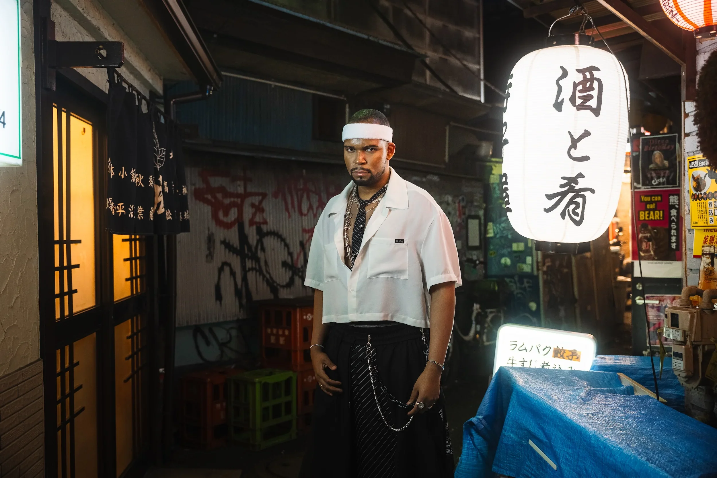Man posing in a traditional lantern-lit Tokyo alley during a professional street style photoshoot
