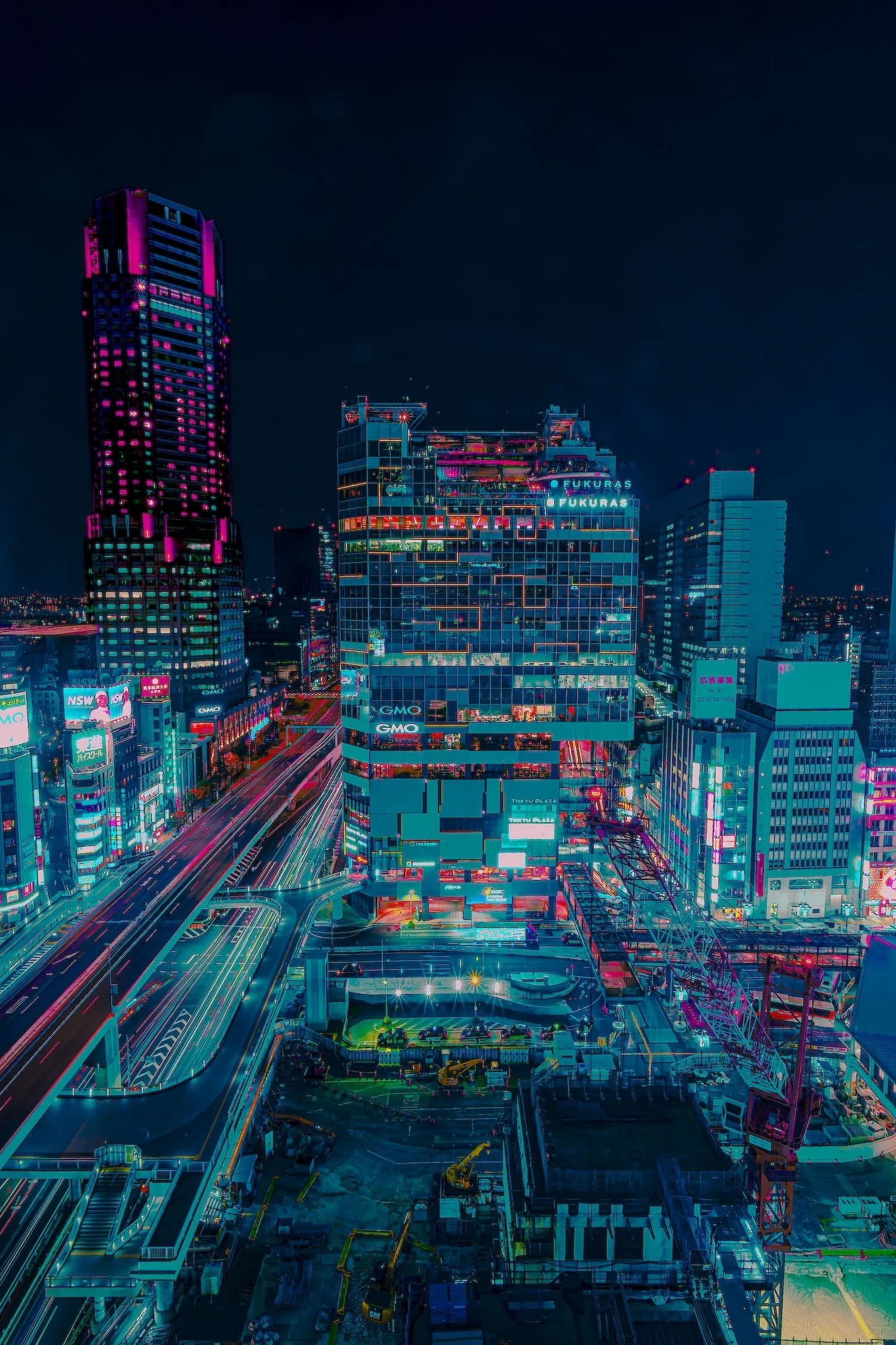 Nighttime cityscape with illuminated skyscrapers in vibrant neon pink and blue lights, construction site with cranes, and busy highways with streaks of moving traffic.