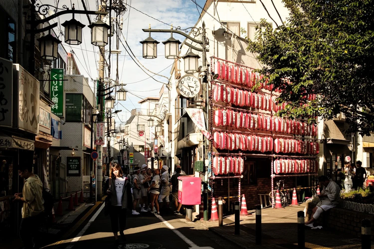 A busy street scene in Japan with pedestrians, shop signs, and a wall of red and white paper lanterns.