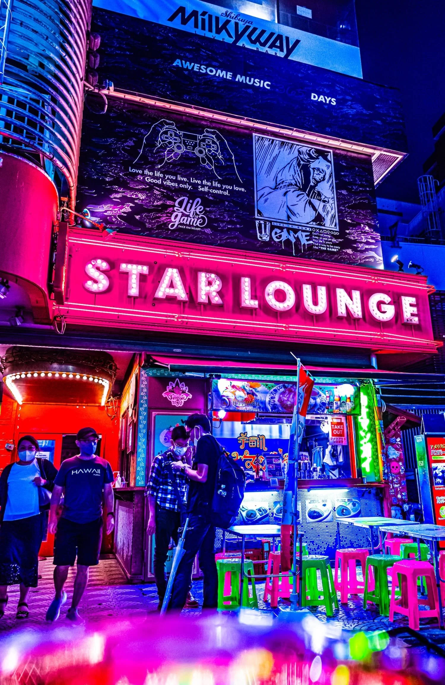 Night scene in front of a neon-lit bar called Star Lounge with colorful stools, people wearing masks, and vibrant signs and advertisements in an urban setting.