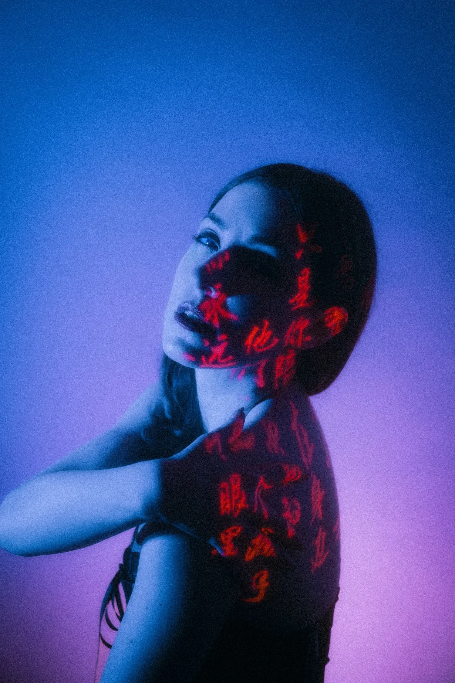 A woman in a dark top with red Chinese characters, looking to the side with a serene expression, against a blue and purple background, with red Chinese text projected onto her face and body.